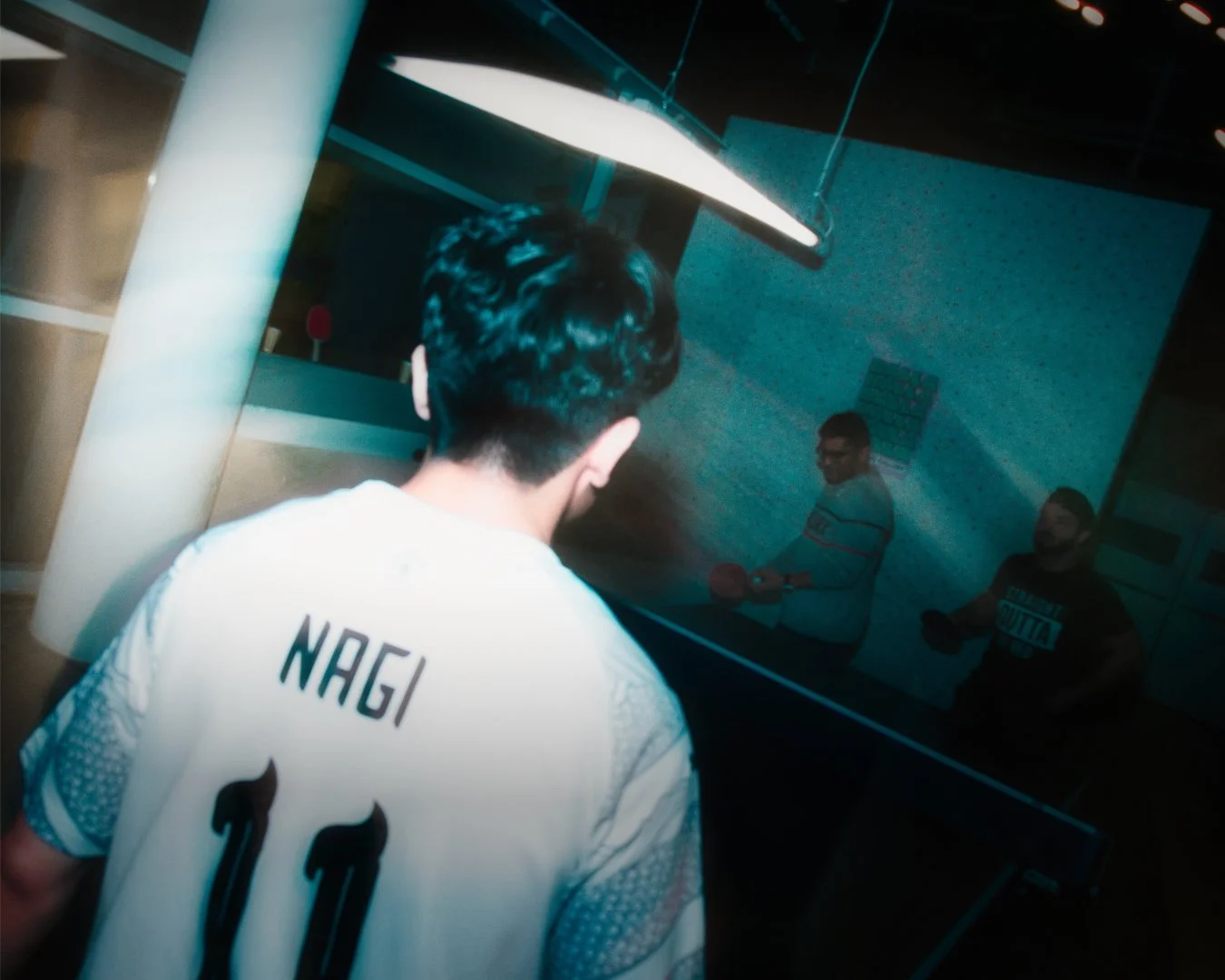 Junger Mann in einem weißen Trikot mit dem Namen NAGI und der Nummer 10, der an einem Tisch im Freizeitcenter Tischtennis spielt