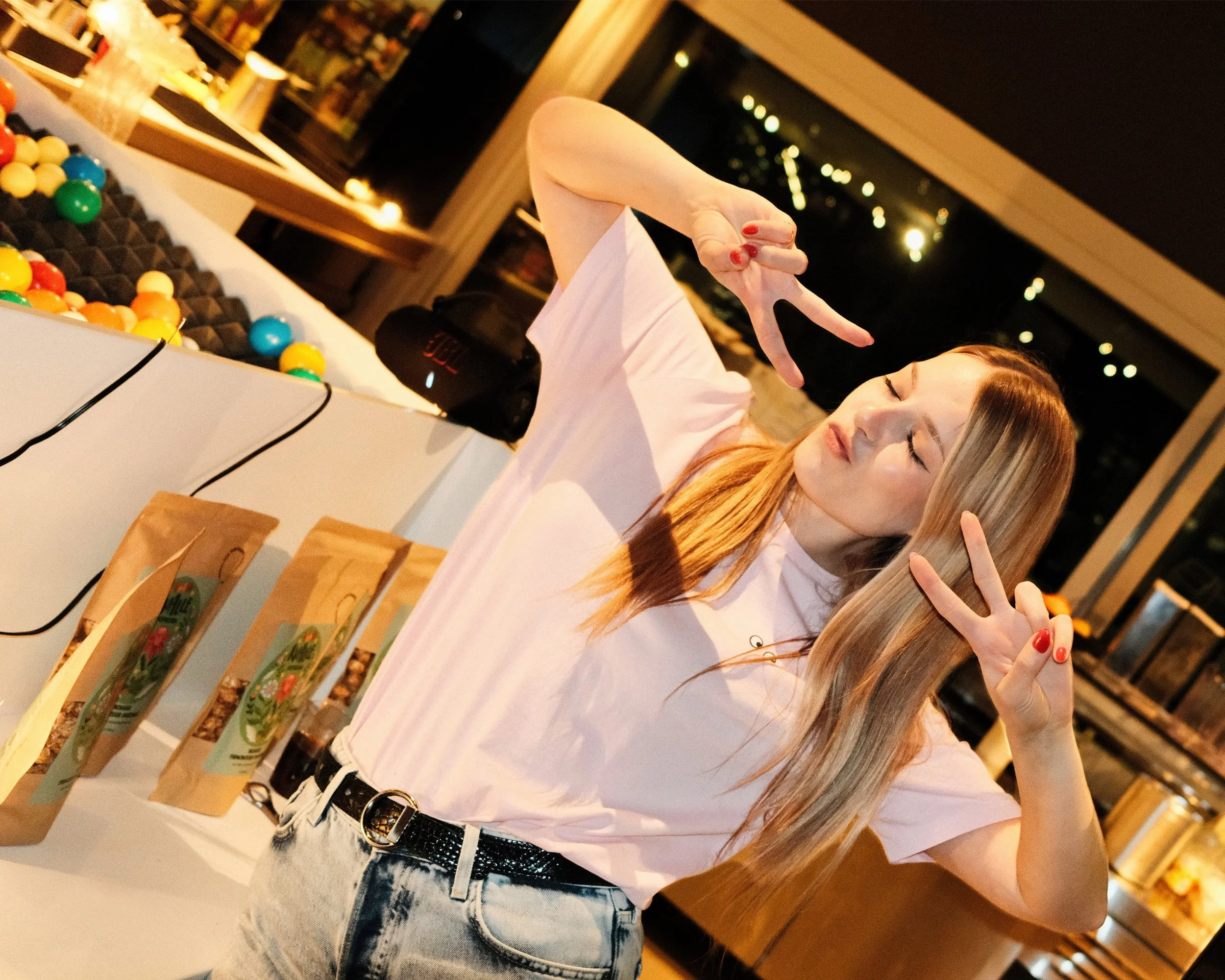Junge Frau mit lange blonden Haaren und heller Haut, trägt eine weiße T-Shirt und Jeans, macht Peace-Zeichen mit den Händen