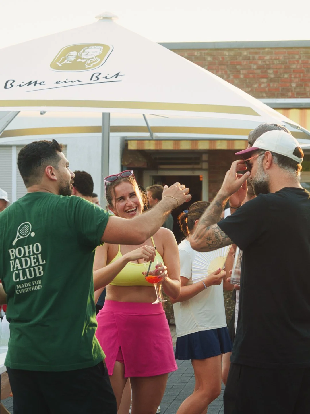 Freunde, die auf einer Party im Freien lachen und sich unterhalten, mit einem großen Sonnenschirm im Hintergrund