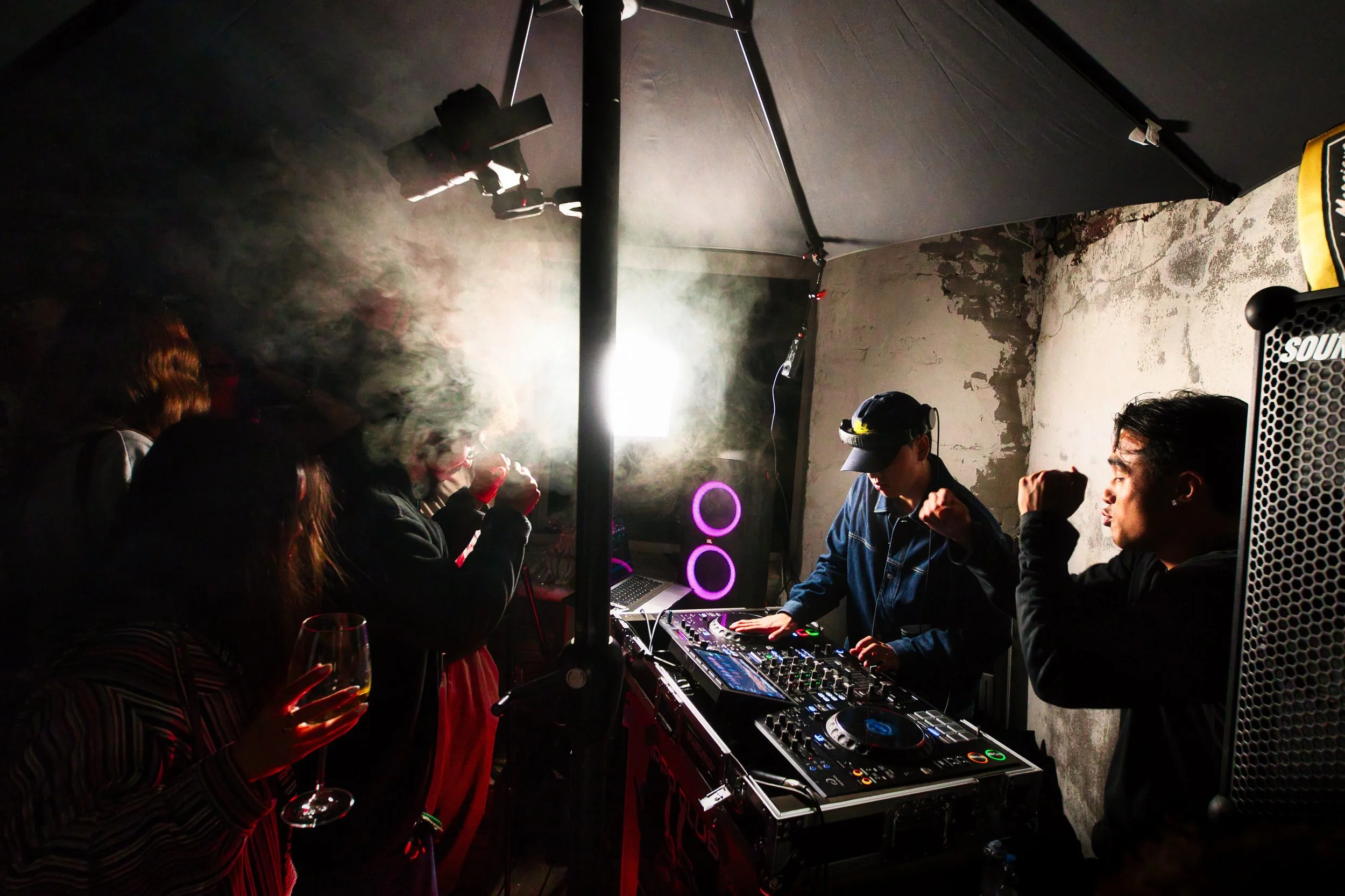 Menschen feiern in einem dunklen Raum mit DJ-Equipment, Rauch und Gesellschaft