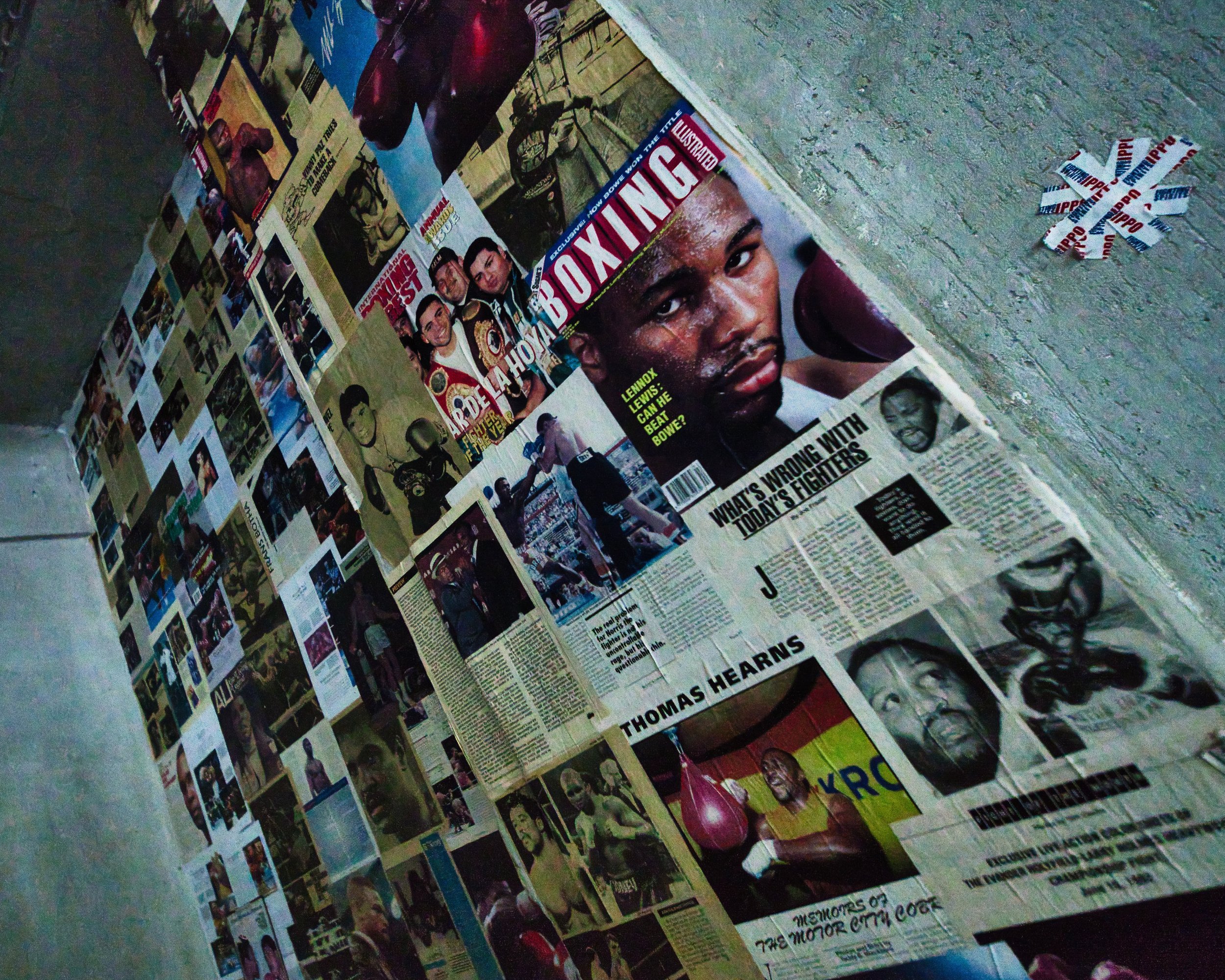 Ein zusammengeklebtes Zeitungs- oder Magazin-Collage an einer Wand mit verschiedenen Bildern und Texten, darunter ein Porträt eines Mannes mit dunkler Haut und schwarzen Haaren, sowie andere Menschen und Szenen.
