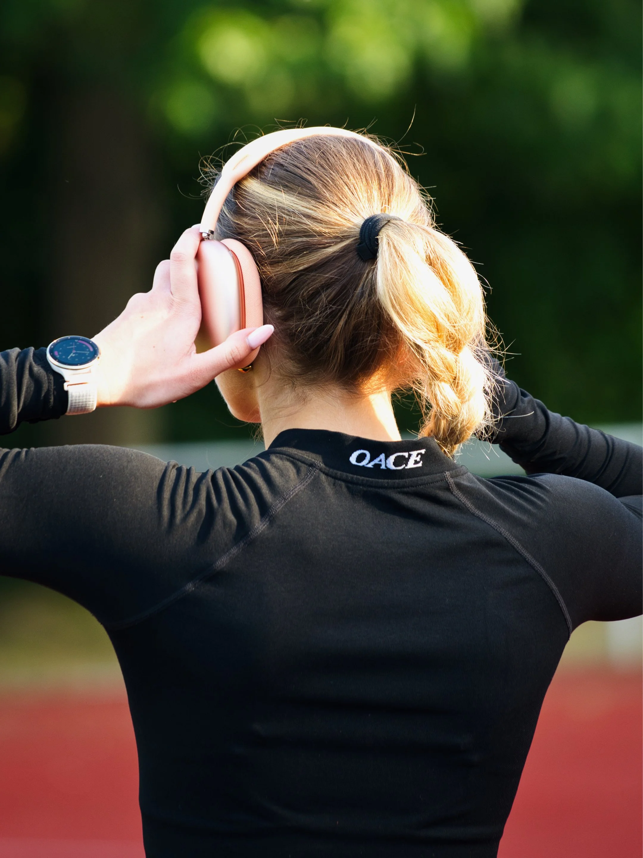 Eine Frau trägt Kopfhörer und ein Sportshirt, vermutlich während eines Trainings im Freien