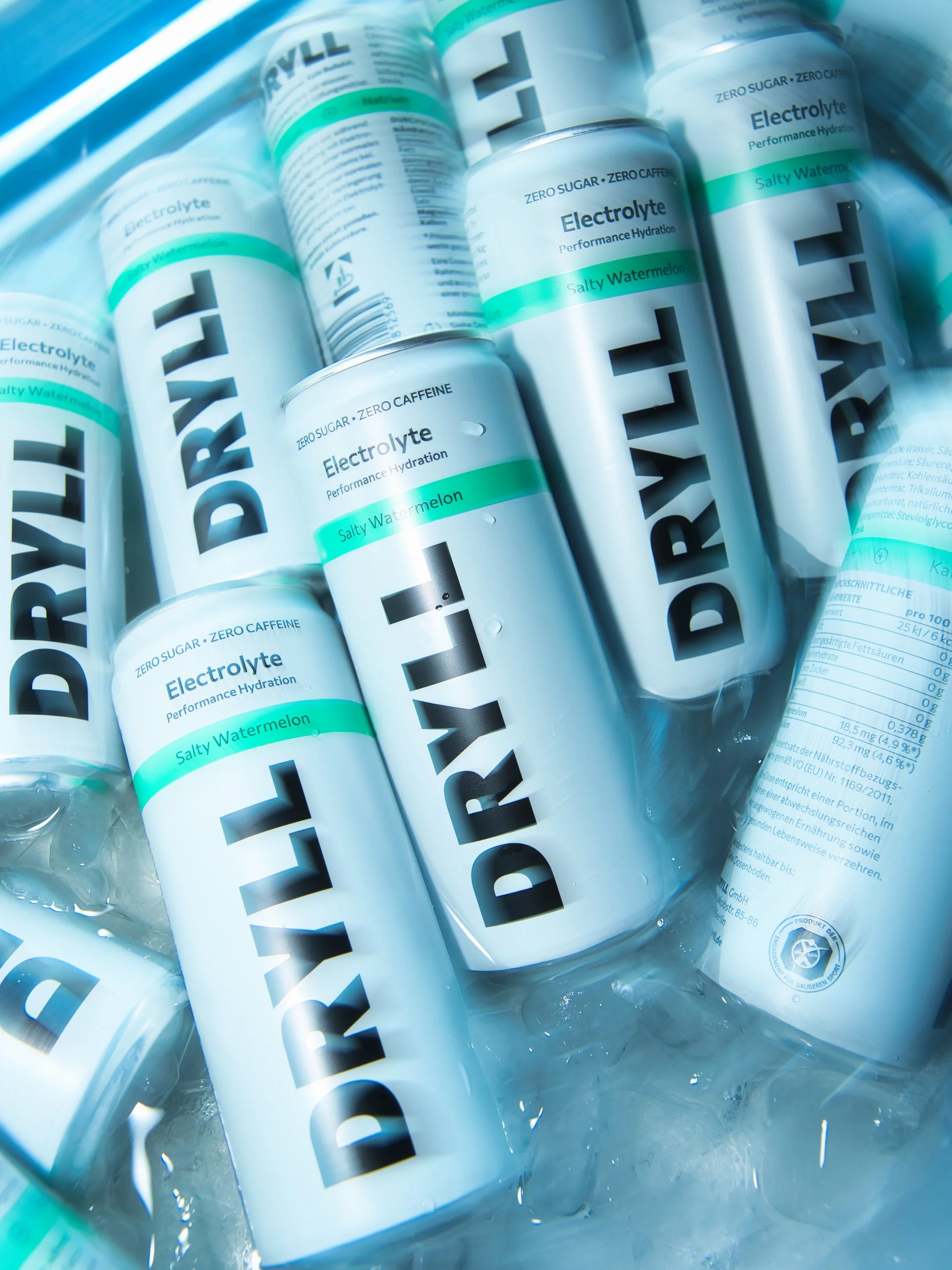 Mehrere Aluminiumdosen mit Wasser, die das Label 'Hydrate' tragen, liegen in einer mit Wasser gefüllten Schüssel. Die Dosen sind von der Marke 'DRYLL' und enthalten Elektrolyt-Getränke mit Geschmack 'Salty Watermelon'