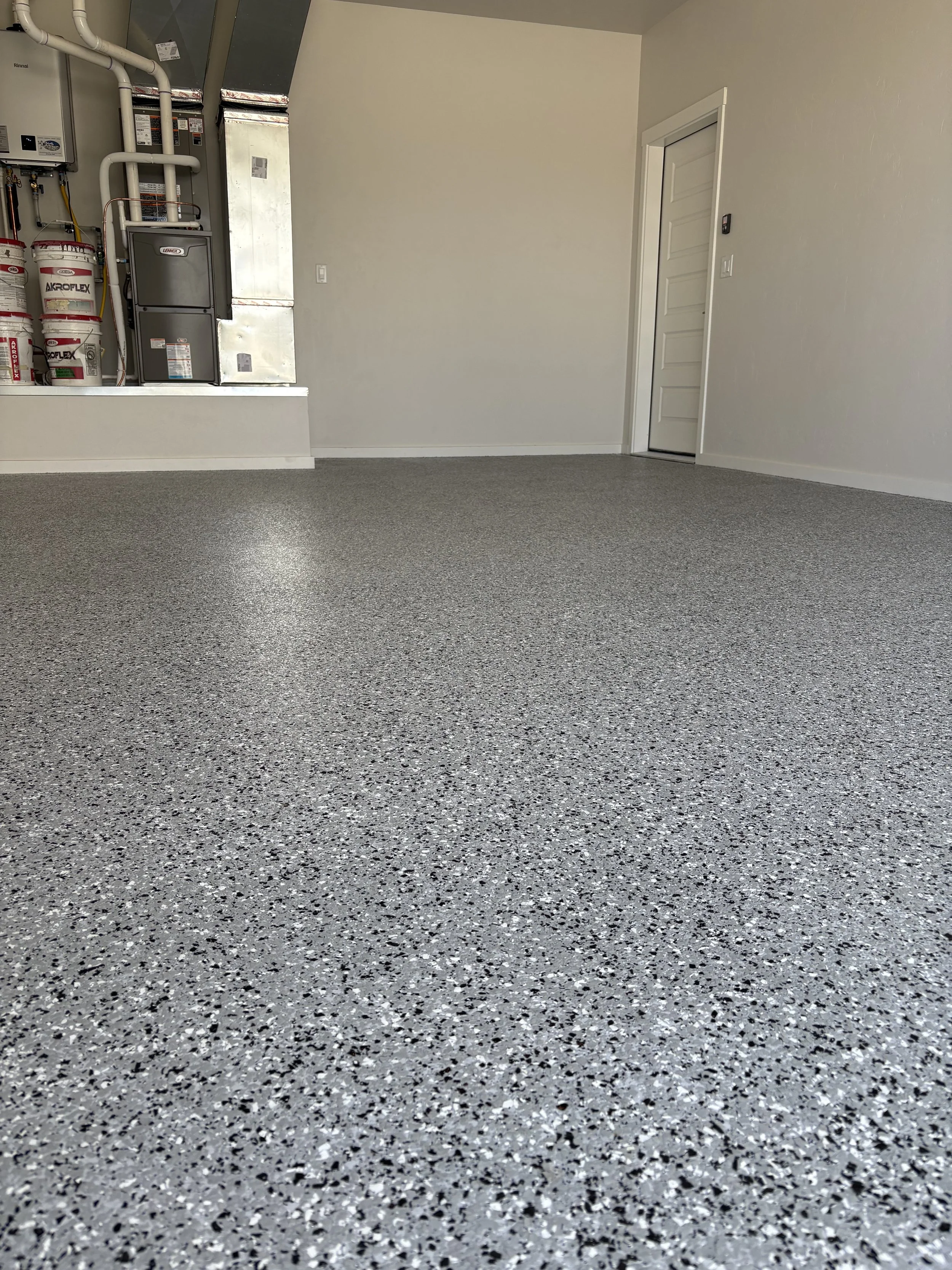 Empty garage with speckled gray epoxy floor, white walls, and a closed white door.