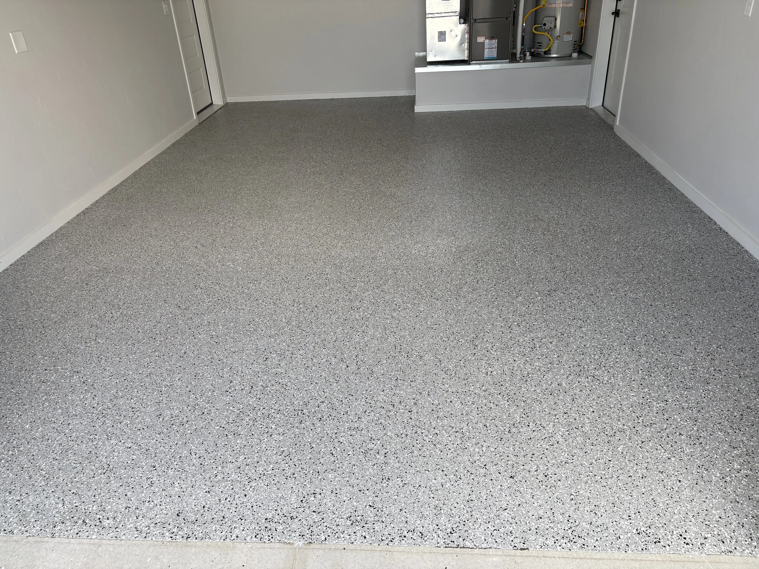 Interior of a room with white walls, grey speckled epoxy flooring, and an HVAC or utility unit installed in a recessed space on the right wall.