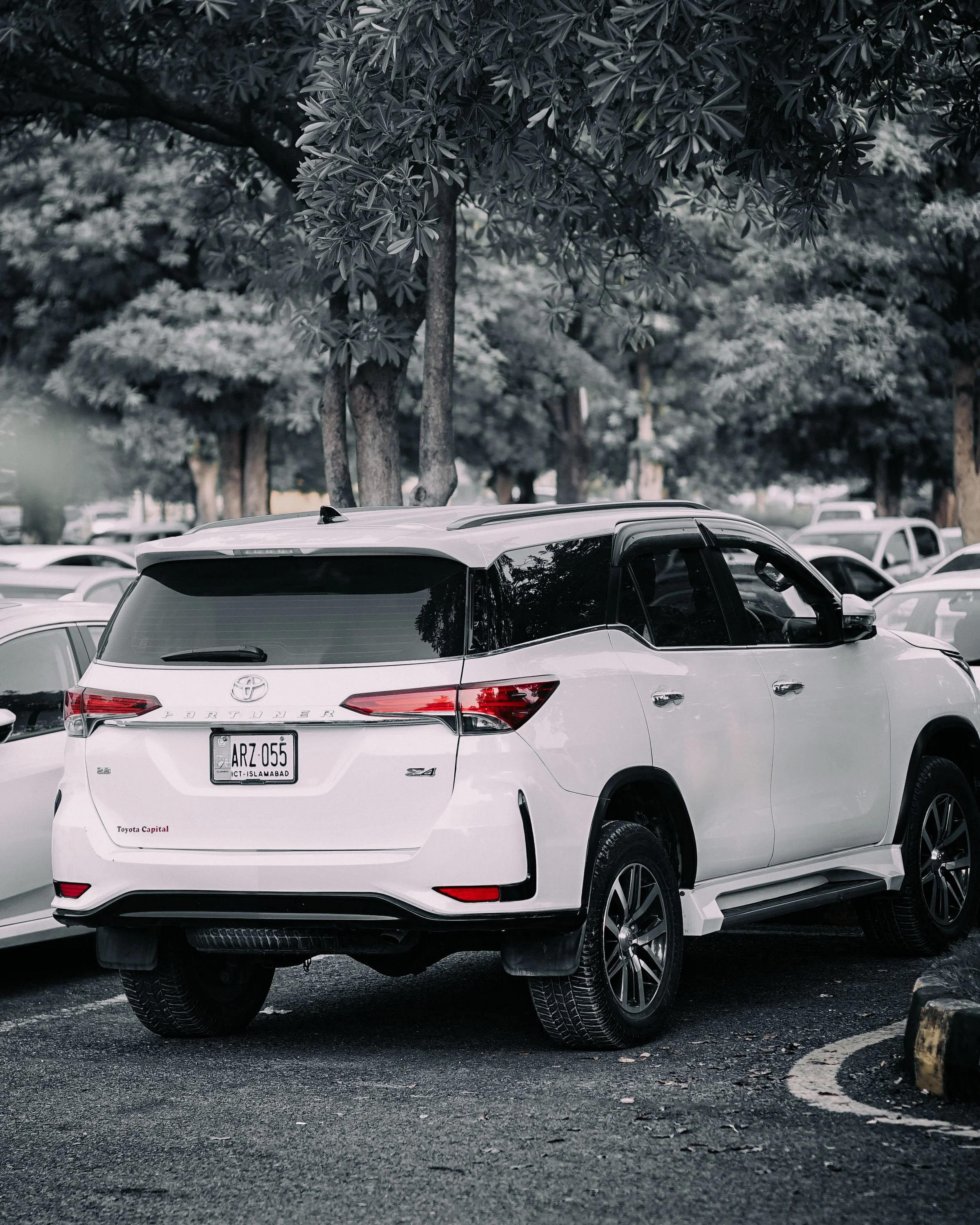 A white Toyota SUV parked in a lot, with trees in the background and other vehicles partially visible around it.
