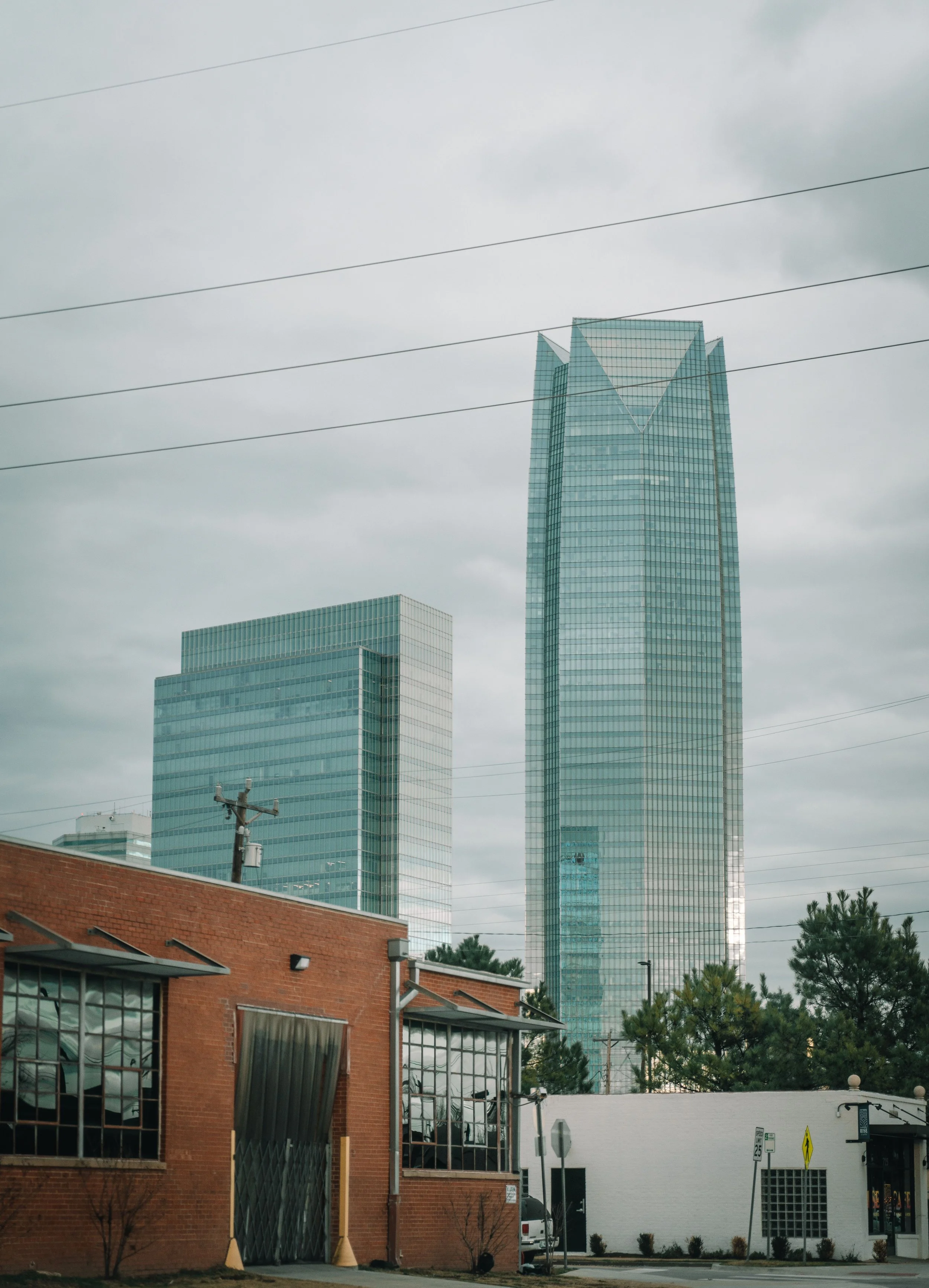 Cityscape featuring modern glass skyscrapers behind a brick building and some trees on an overcast day.