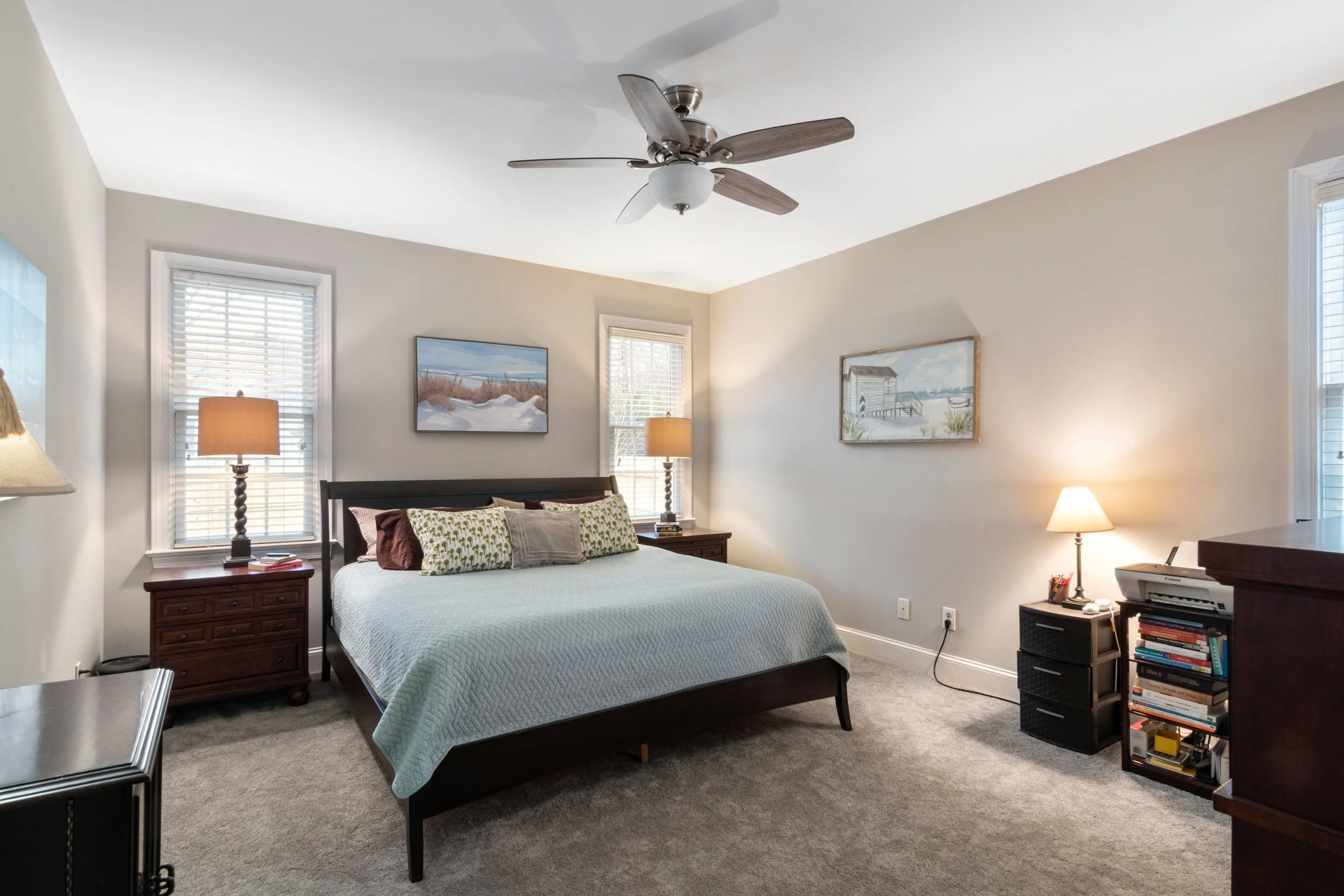 A bedroom with a bed, nightstands, lamps, and artwork on the walls.