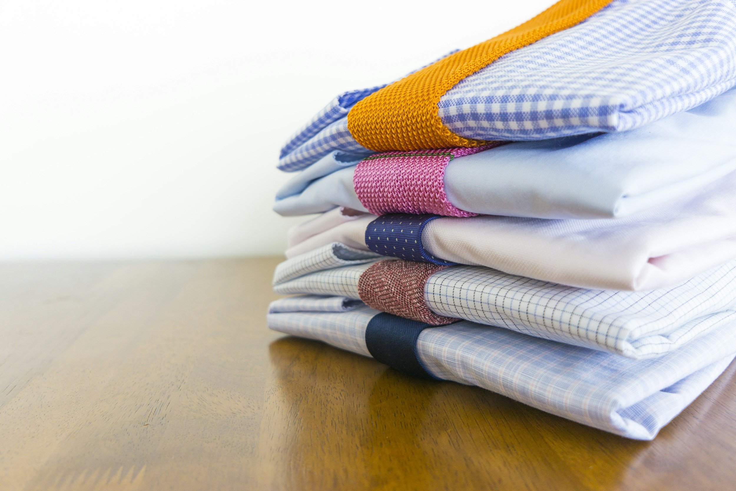 Stack of neatly folded button-up shirts with various patterns and colors on a wooden surface.