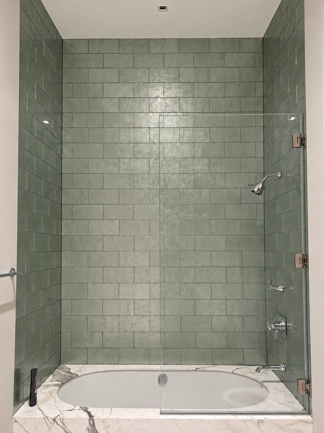 Empty modern bathroom shower with green tiles, a built-in bathtub, and a marble ledge, viewed from the front.