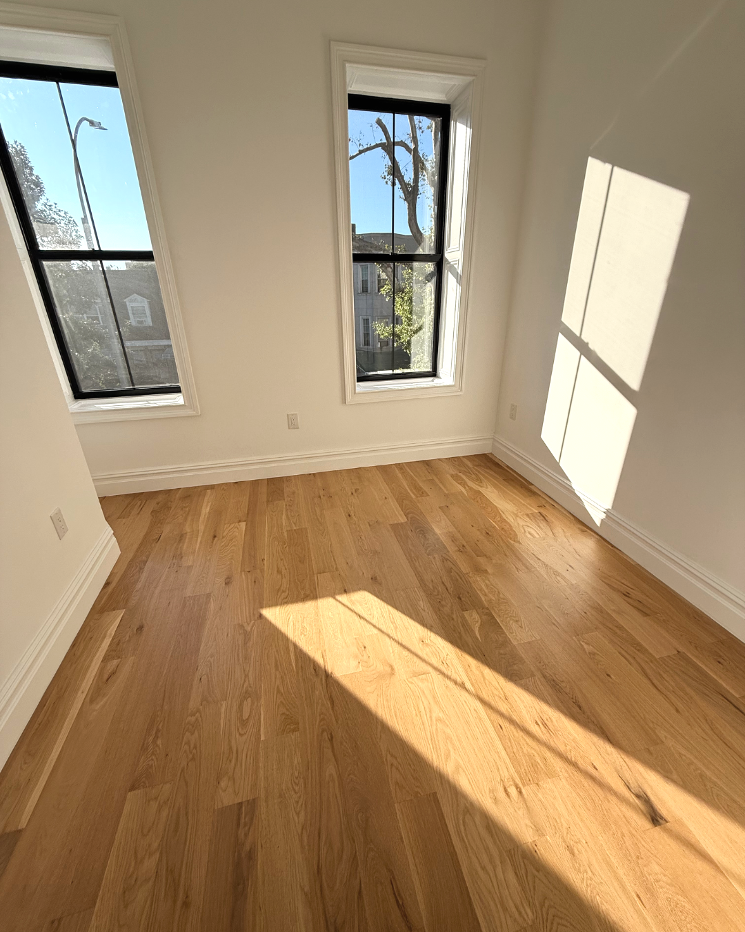 Empty sunlit room with hardwood floors.