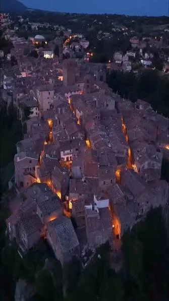 Veduta aerea di un borgo storico di case in pietra con luci calde, in collina di sera.