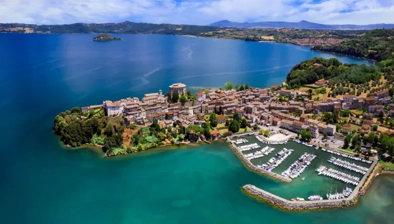 Veduta aerea di un paese vicino a un lago con un porto turistico e un castello storico.