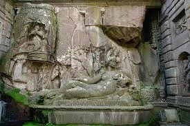 Scultura di un drago o creatura fantasy su una piattaforma di pietra, con dettagli intricati, parte di un monumento storico o decorativo.