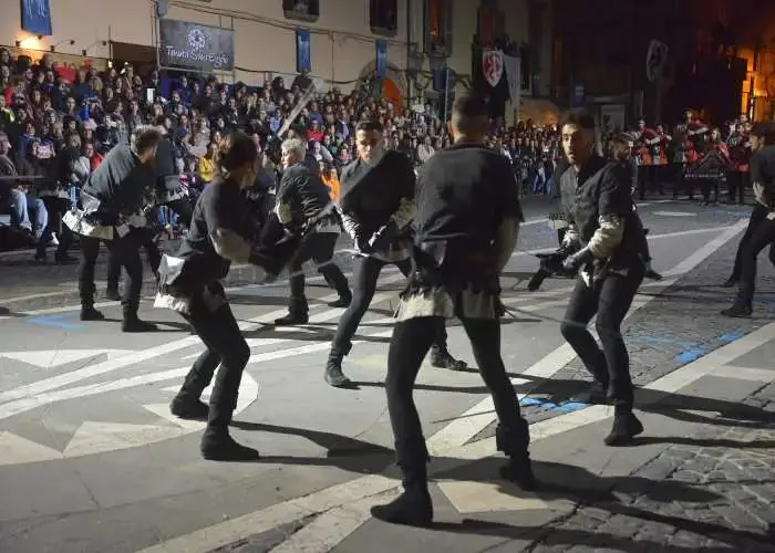 Gruppo di persone che ballano una danza tradizionale in strada davanti a una folla di spettatori.