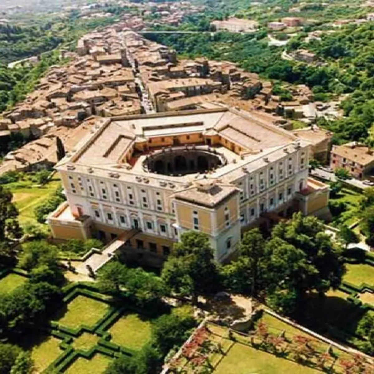 Vista aerea di un grande edificio storico circondato da giardini e case nei dintorni.