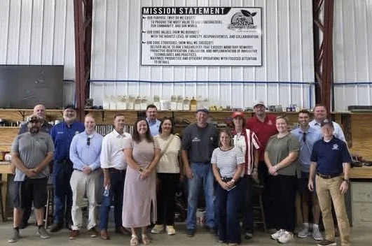 Group of people standing in a line inside an industrial building with a mission statement sign above them.