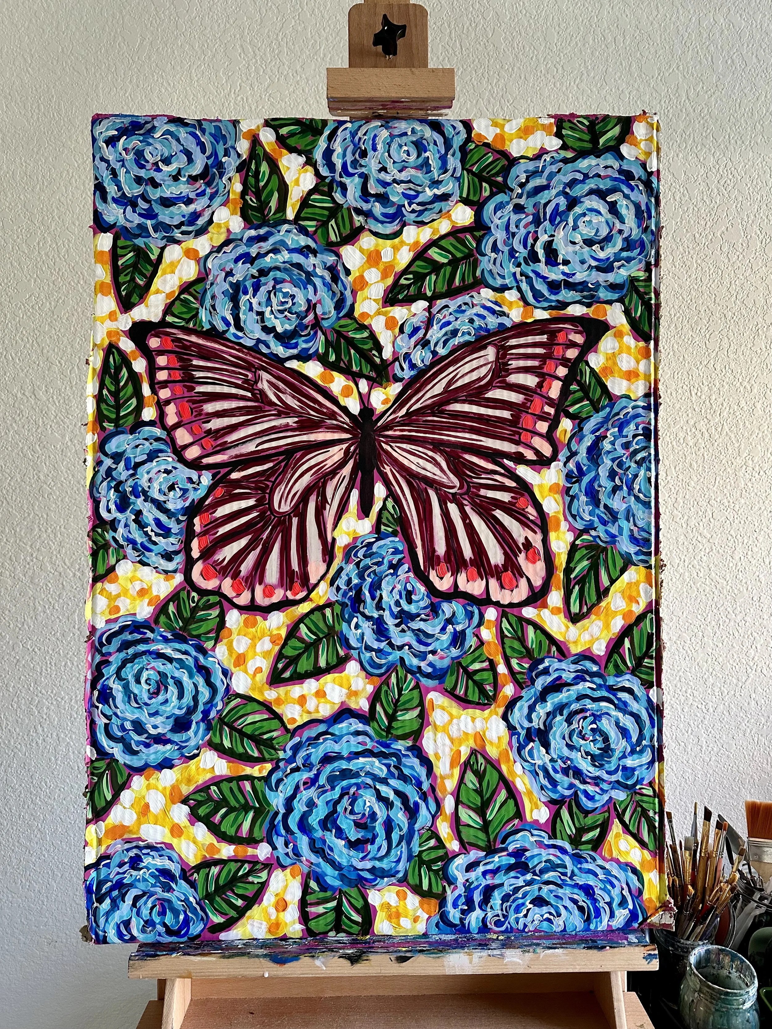 Neon and maroon butterfly painting on cardboard with bright blue flowers.