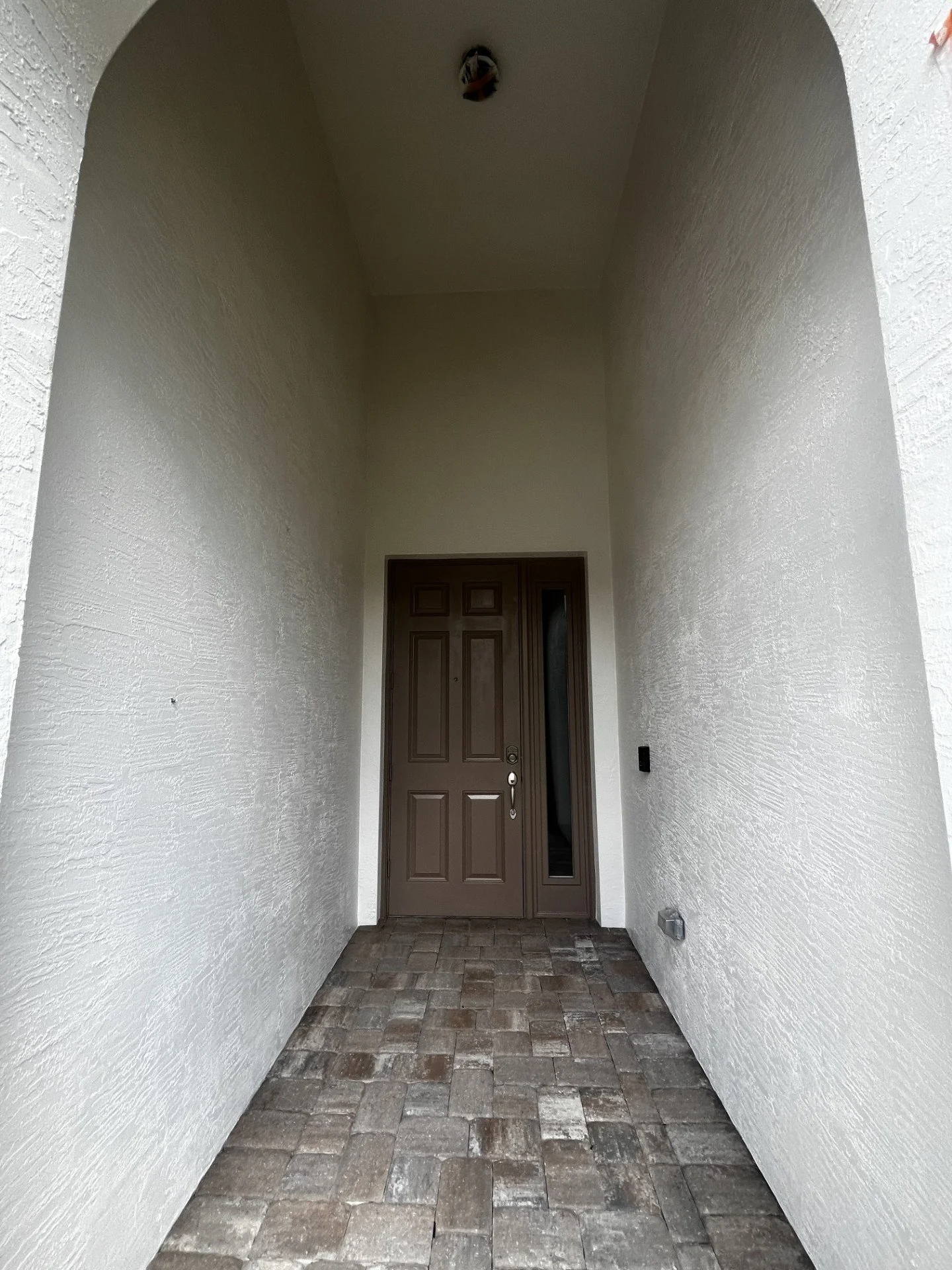 Entrance with a brown door, textured white walls, a narrow corridor, and a brick floor.