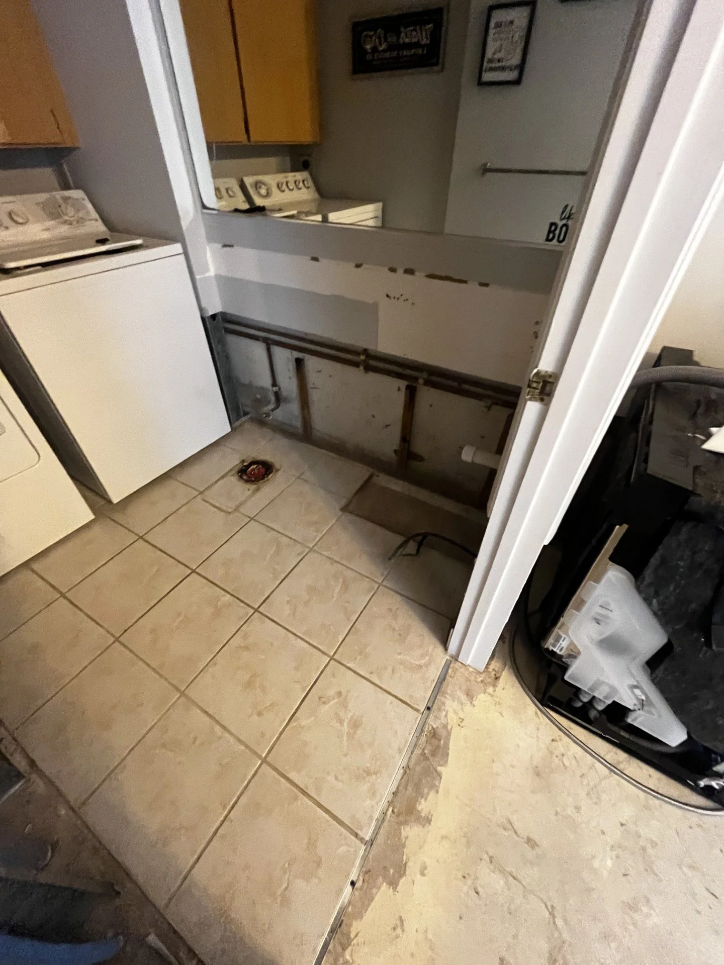 A laundry room with an unfinished space for a washer and dryer, tiled floor, and walls with framed pictures. The washer and dryer are not visible.
