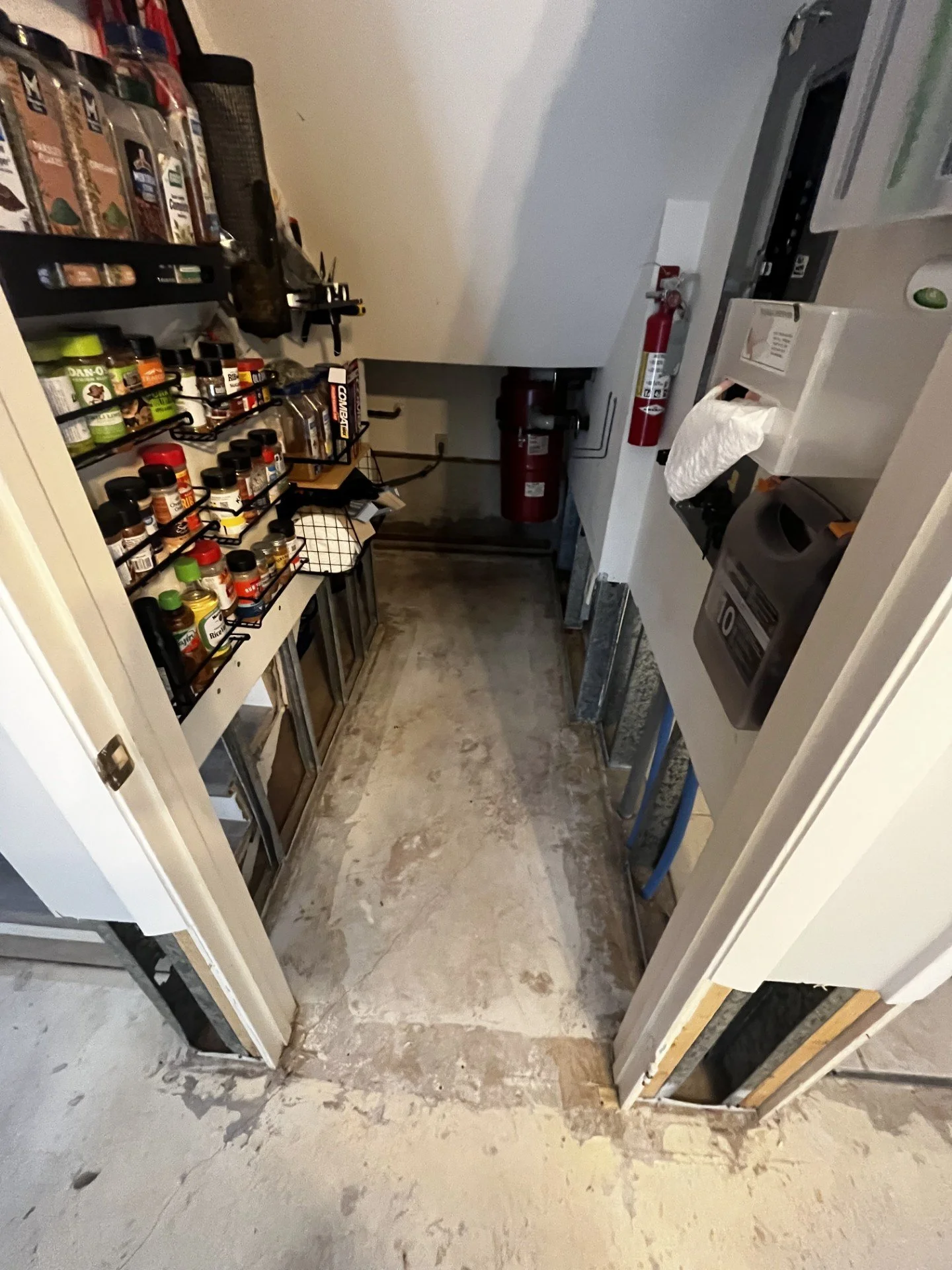A small unfinished utility or laundry room with various supplies, a fire extinguisher, and exposed walls with some organizational storage.