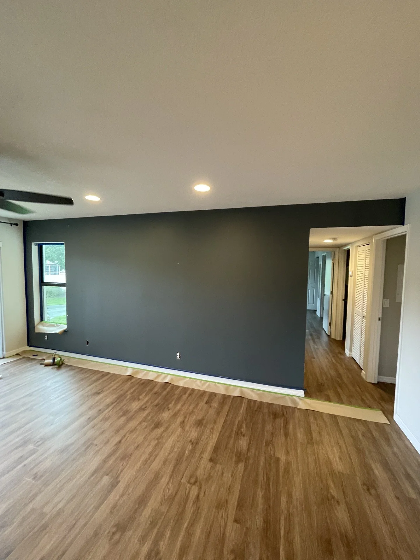 Interior of a house with new wooden flooring, a dark accent wall, and doorway leading to other rooms, with some painting tools on the floor.