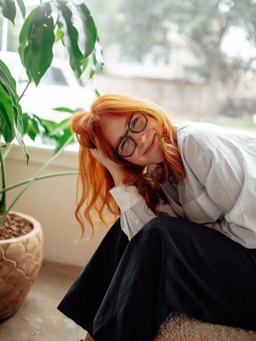 Haleigh Culverhouse, certified Enneagram coach, smiling while seated beside a large houseplant.