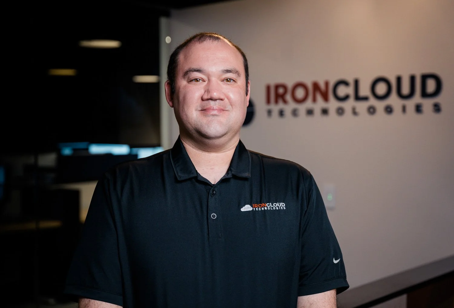 A man in a black polo shirt standing in front of a wall with the IRONCLOUD Technologies logo. He has short dark hair and a slight smile.