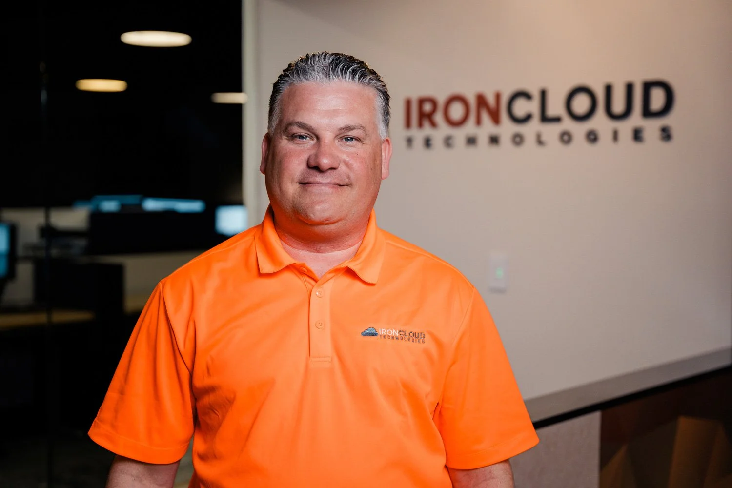 A man in an orange polo shirt standing in front of a wall with the 'IronCloud Technologies' logo.