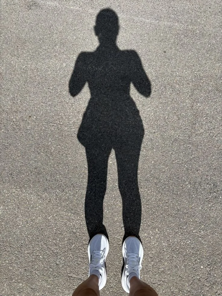 Shadow of a person standing on pavement, wearing sneakers.