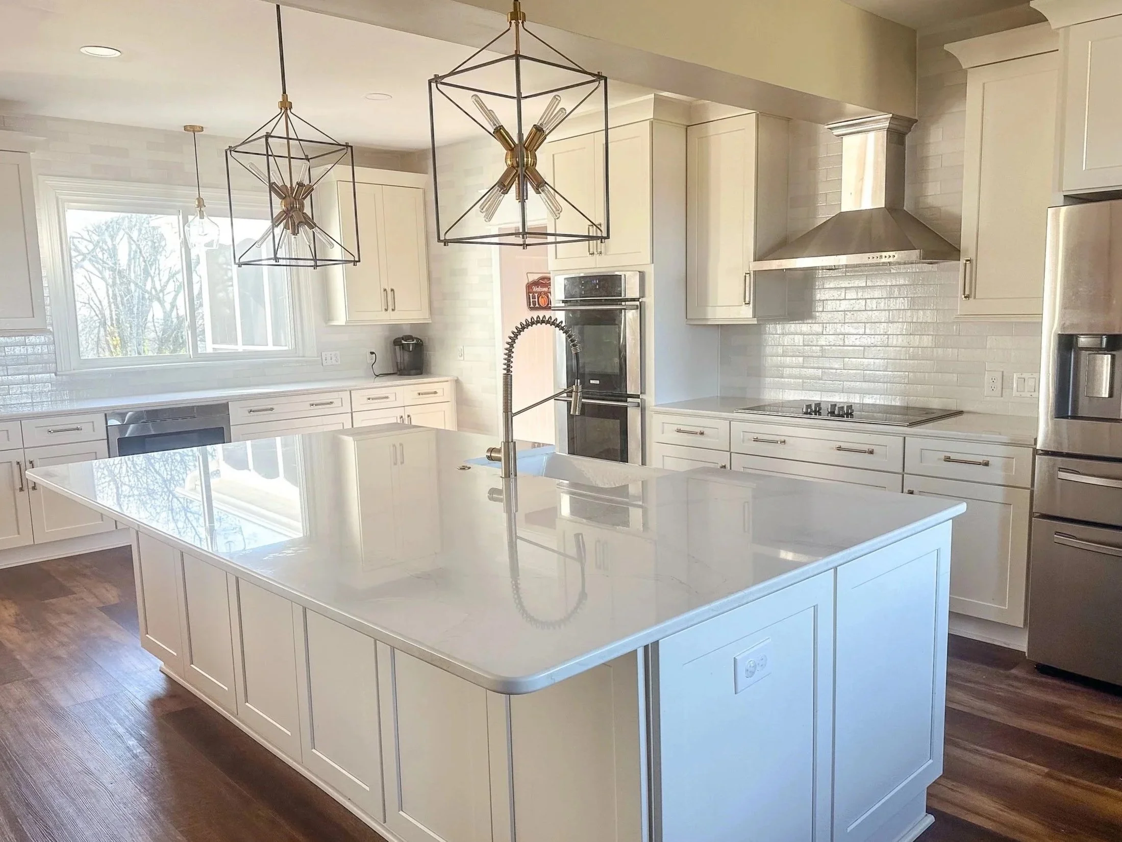 Modern kitchen with white cabinetry, stainless steel appliances, a large white island, and two geometric pendant lights hanging from the ceiling.