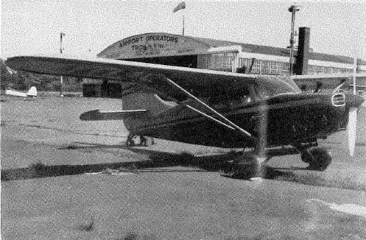 Black and white photo of a small aircraft parked outside a building labeled 'Airport Operations'.