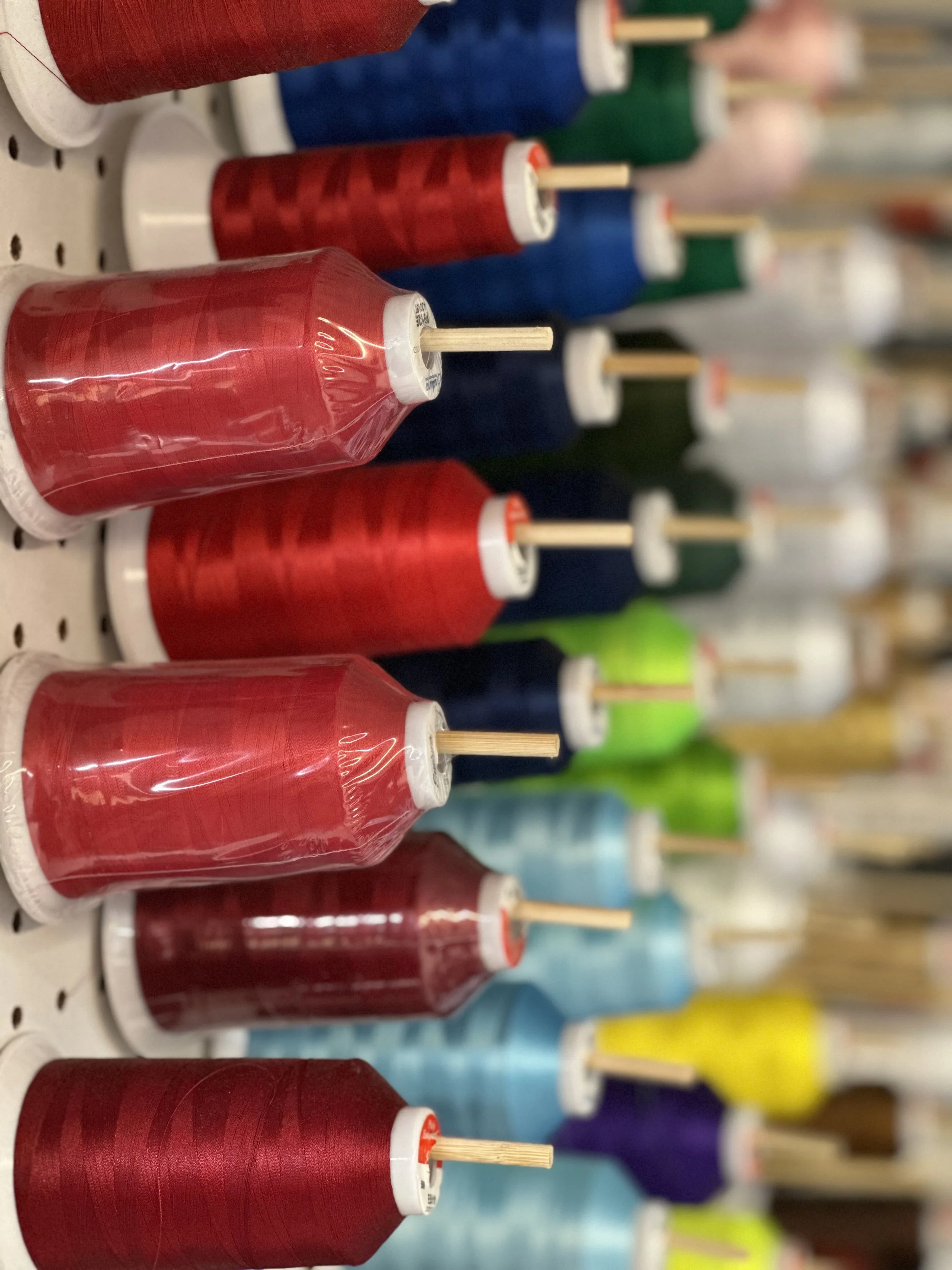 Rows of red, green, blue, and yellow embroidery thread spools with wooden rods, displayed on store shelves.