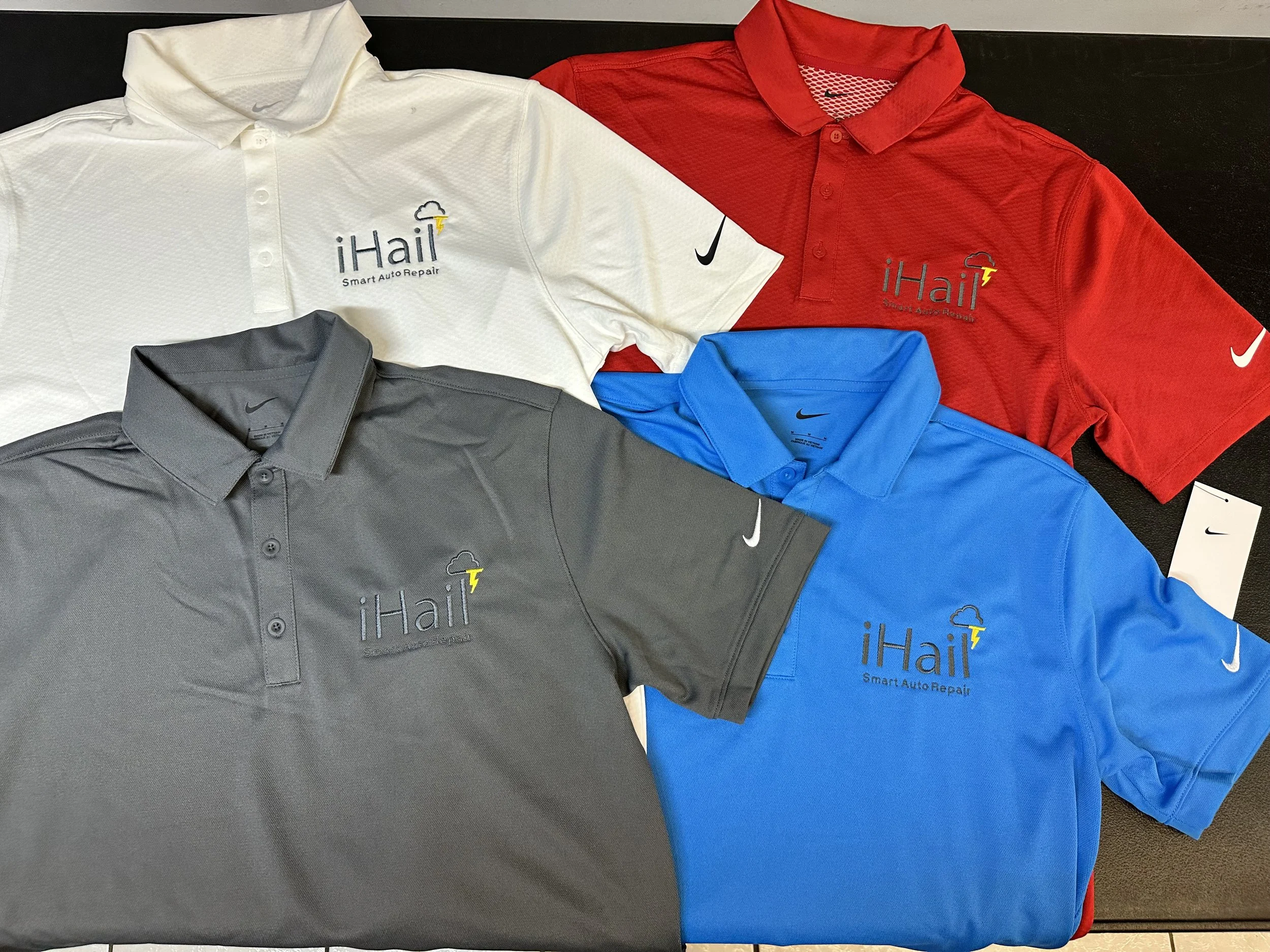 Four collared Nike polo shirts in white, red, gray, and blue with embroidered logos for iHail and Nike, arranged on a flat surface.
