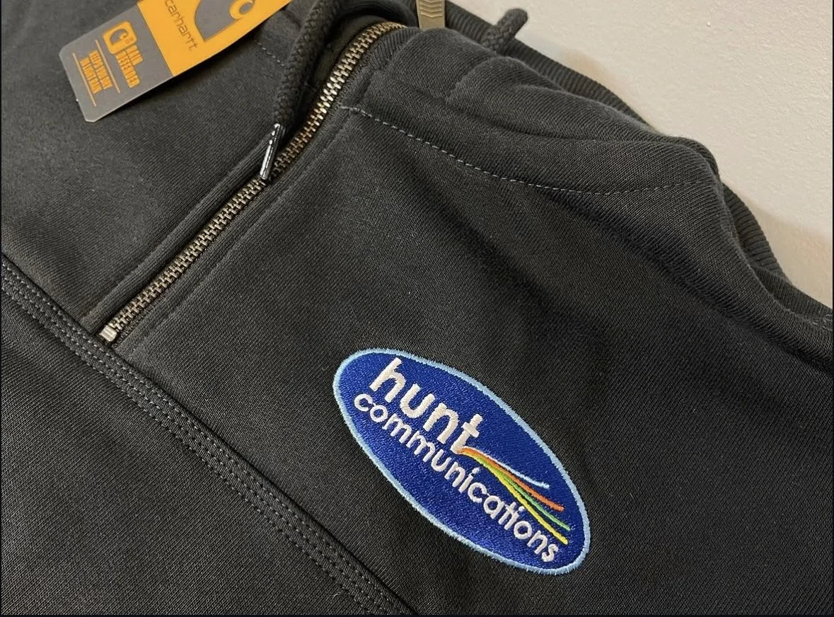 Black Carhartt Jacket with an embroidered blue logo that says "hunt communications" along with fibers in the design