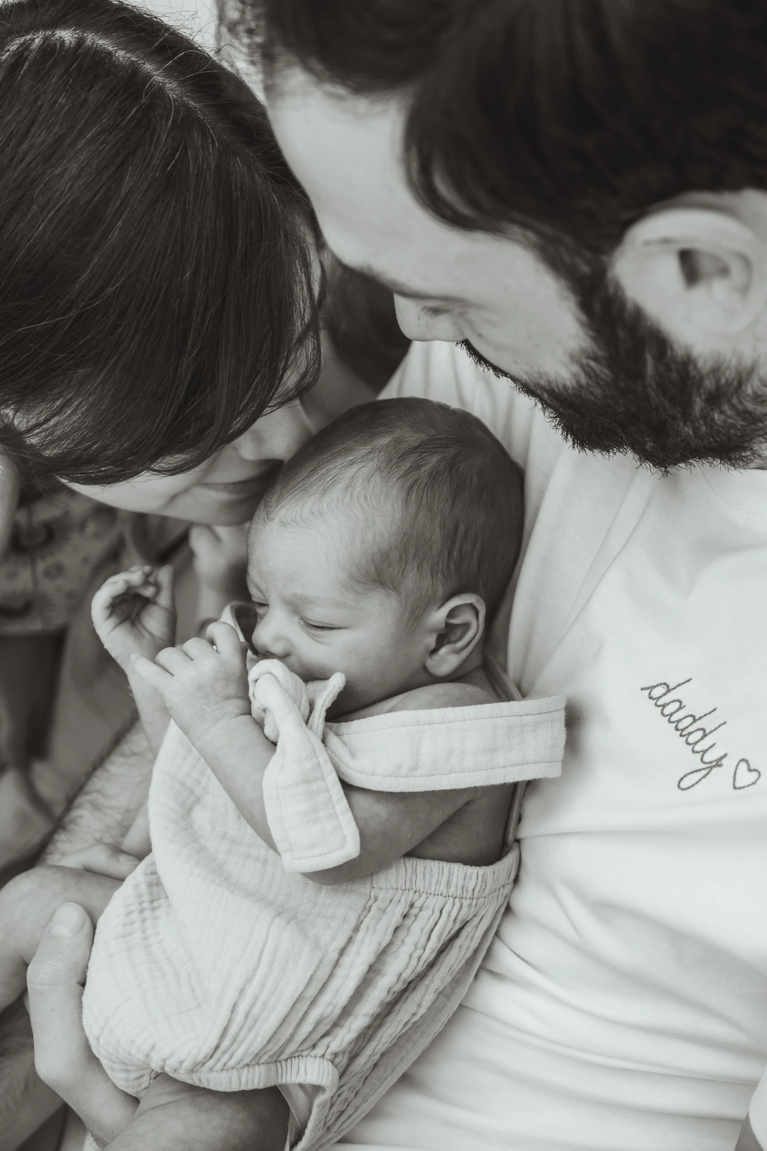A family holding a newborn baby close to their faces, sharing a tender moment.