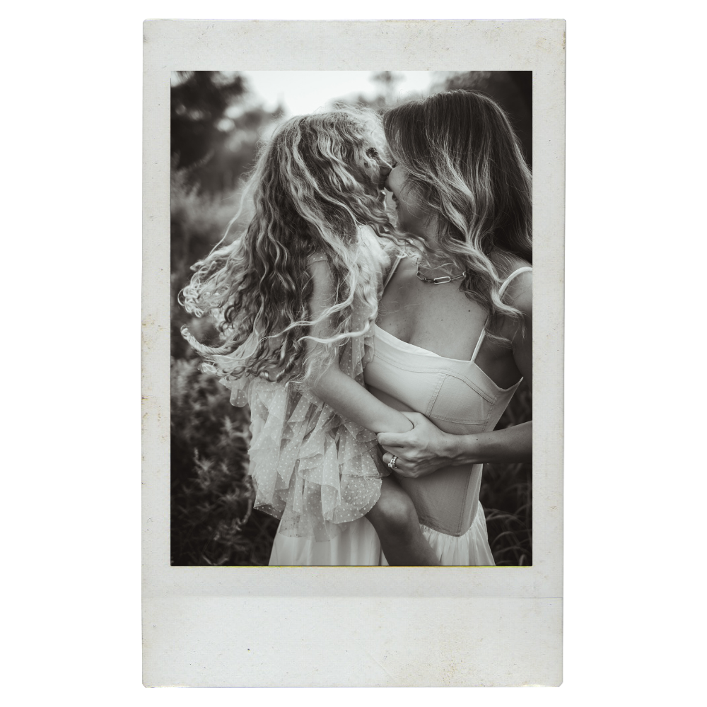 A woman and a young girl sharing an intimate moment outdoors, nose to nose, in black and white. The woman is holding the girl, and both are smiling with their faces close together.