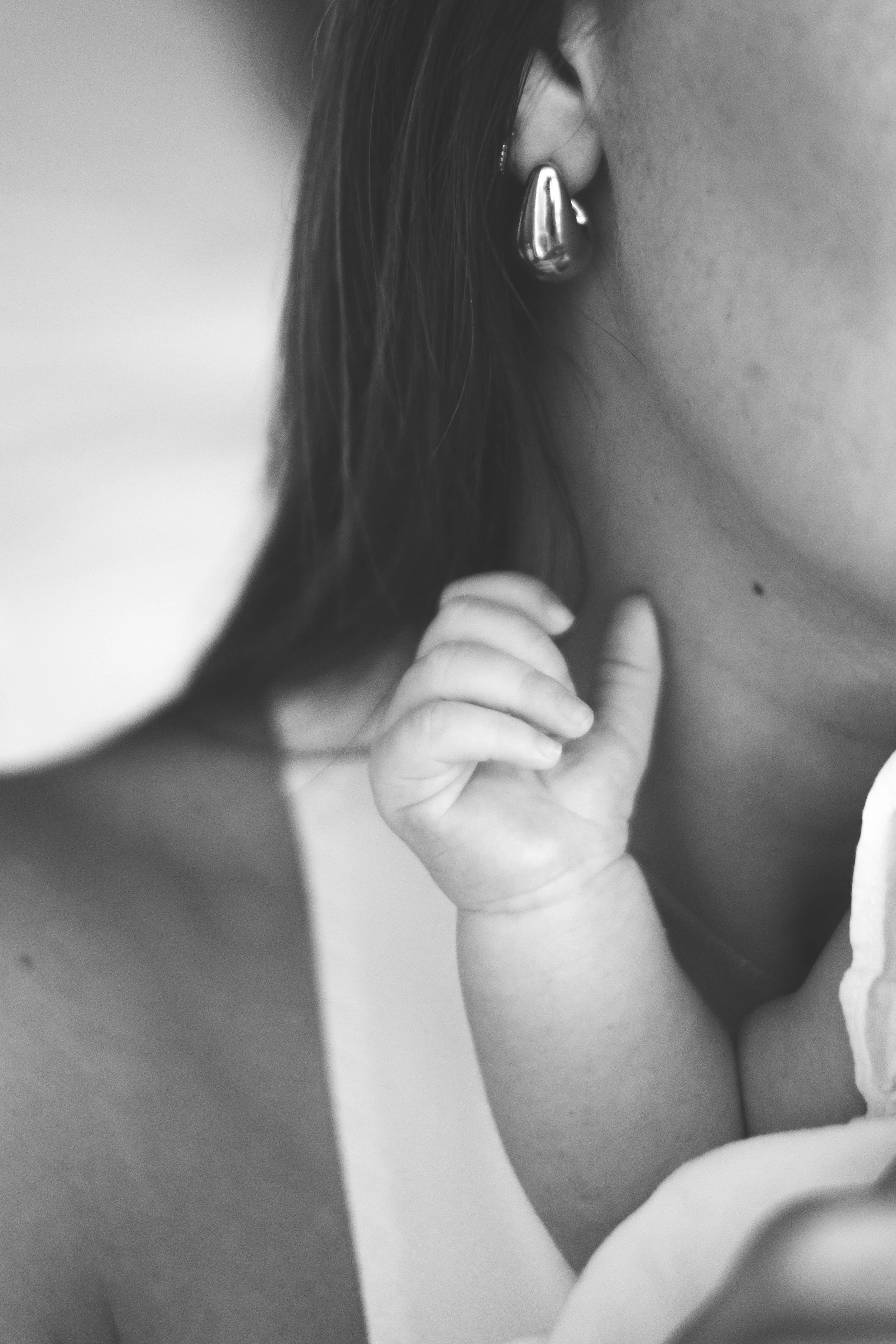 Close-up of a woman with dark hair and earrings, gently touching her neck.