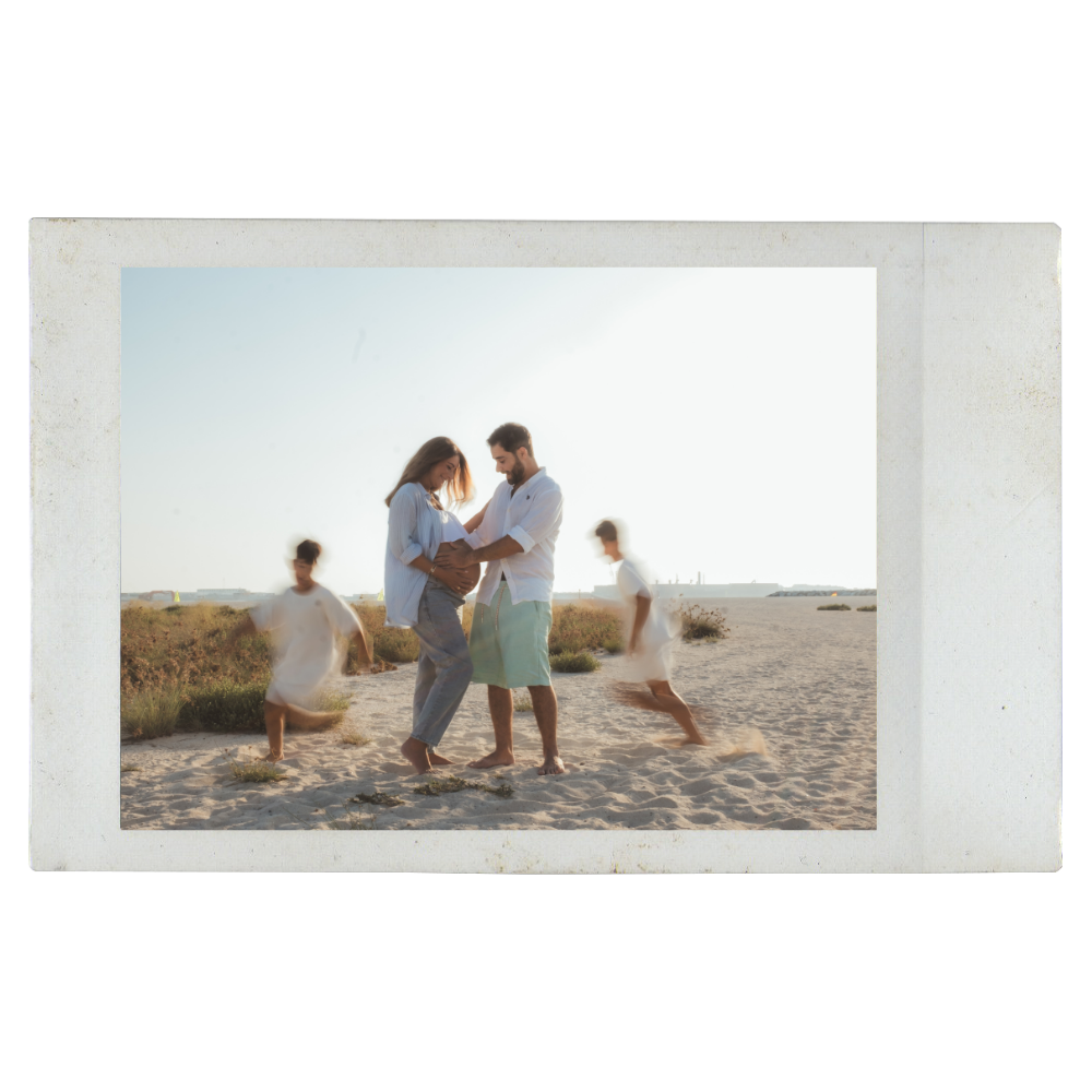 A family at the beach, including a pregnant woman, a man, and two children, with the couple standing close together and children playing around them.