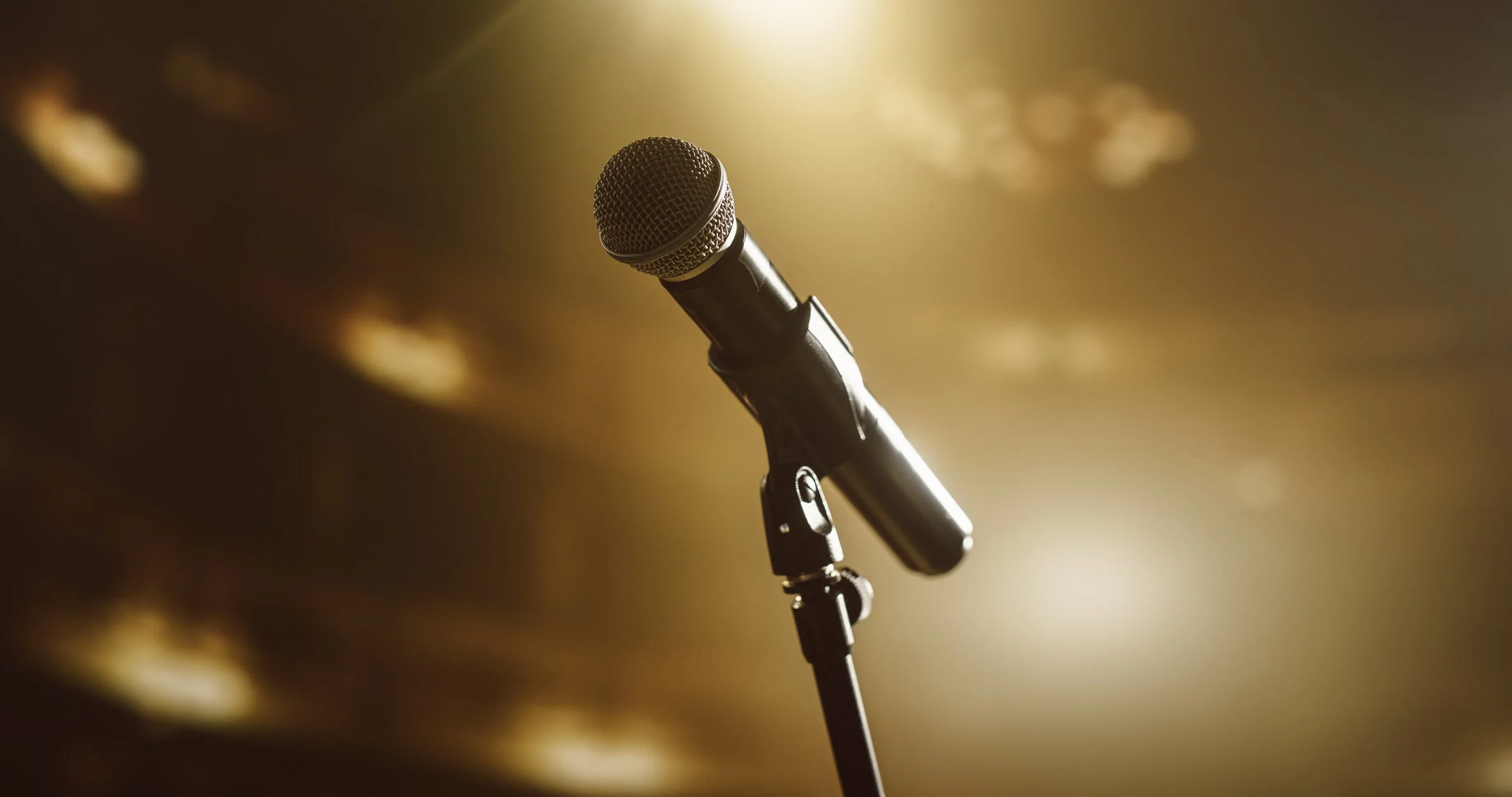 A microphone on a stand with a blurred stage background and warm lighting.