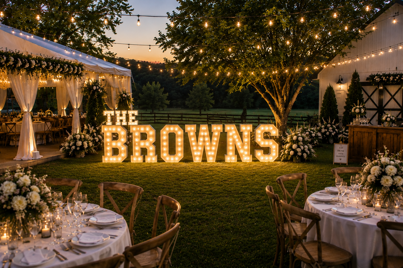 Outdoor wedding reception setup at dusk with large illuminated sign reading 'THE BROWNS', decorated tables, flower arrangements, string lights, and a tree with lights
