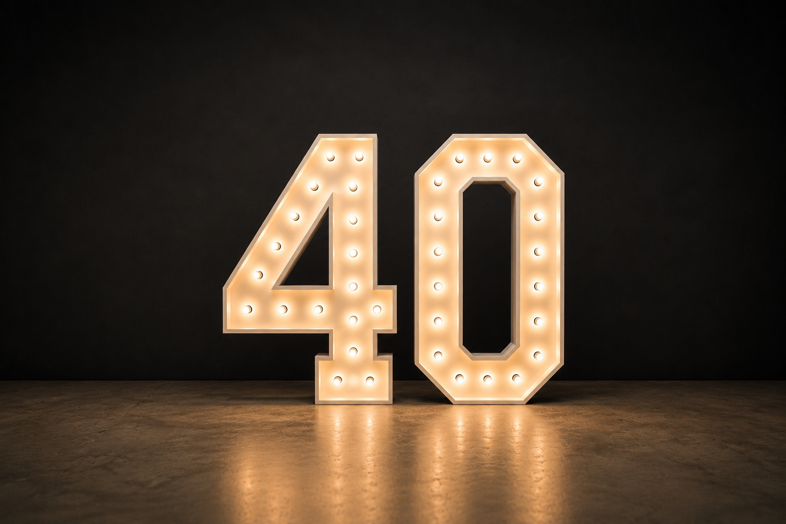 Illuminated number 40 sign with lights on black background and wooden floor.
