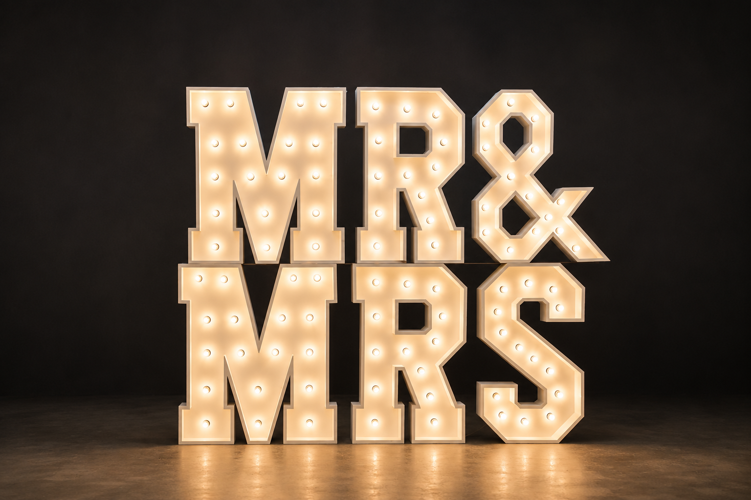 Illuminated sign reading 'MR & MRS' with large block letters and light bulbs, on a dark background.