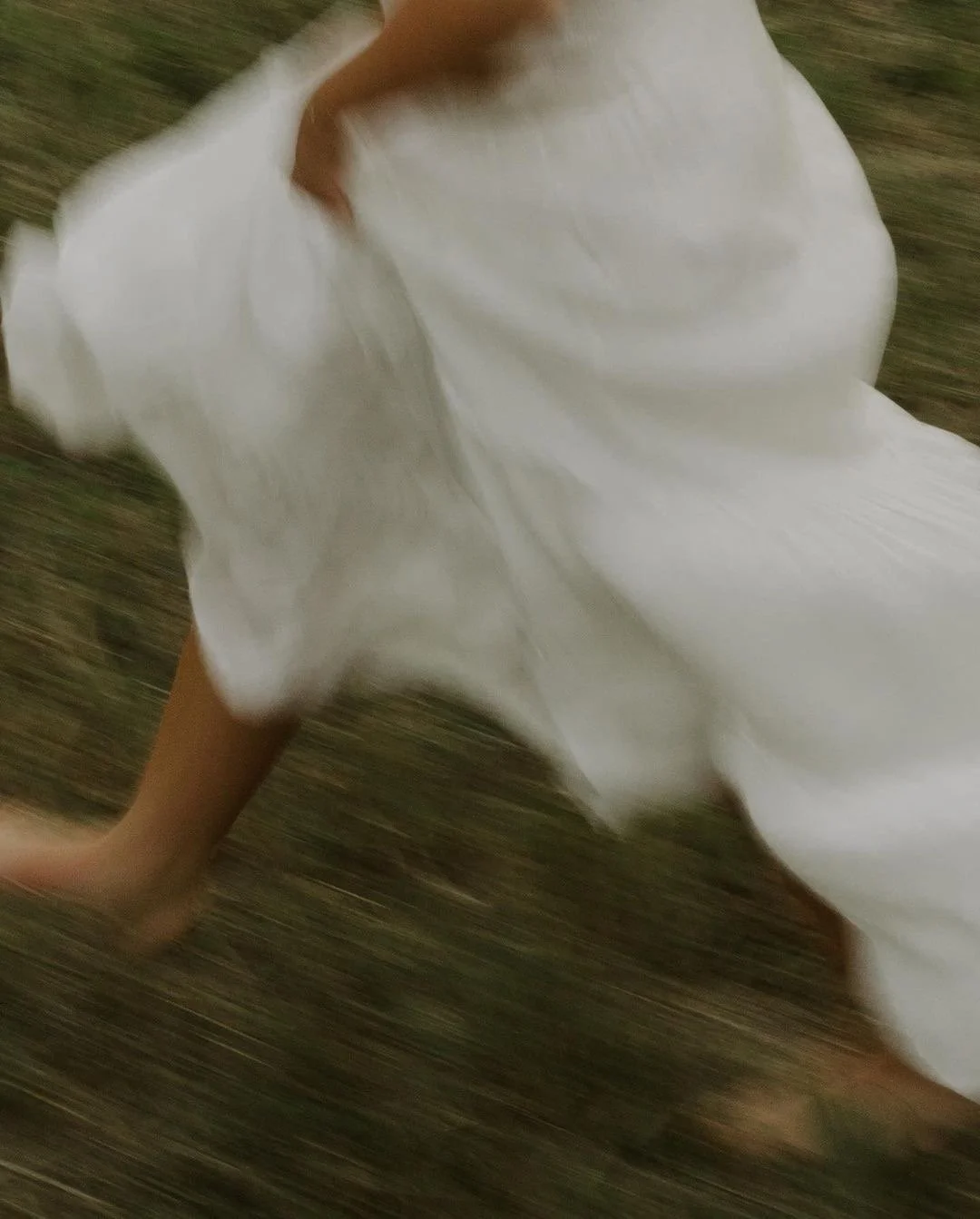 Person wearing a white dress is running or falling on a grassy surface.