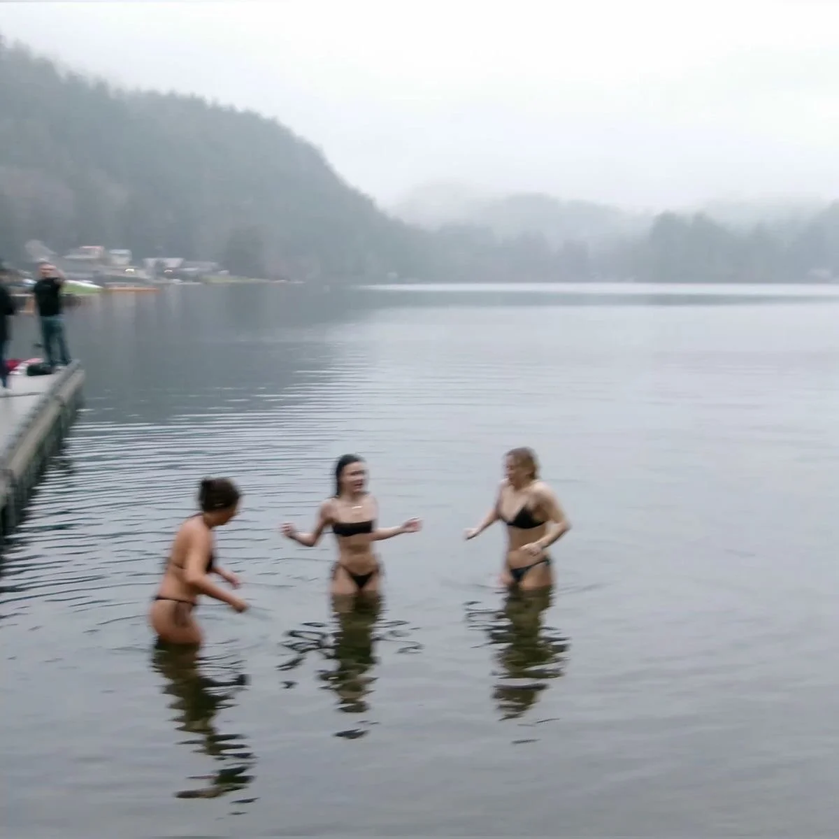 Three women in swimsuits standing in a lake on a foggy day.