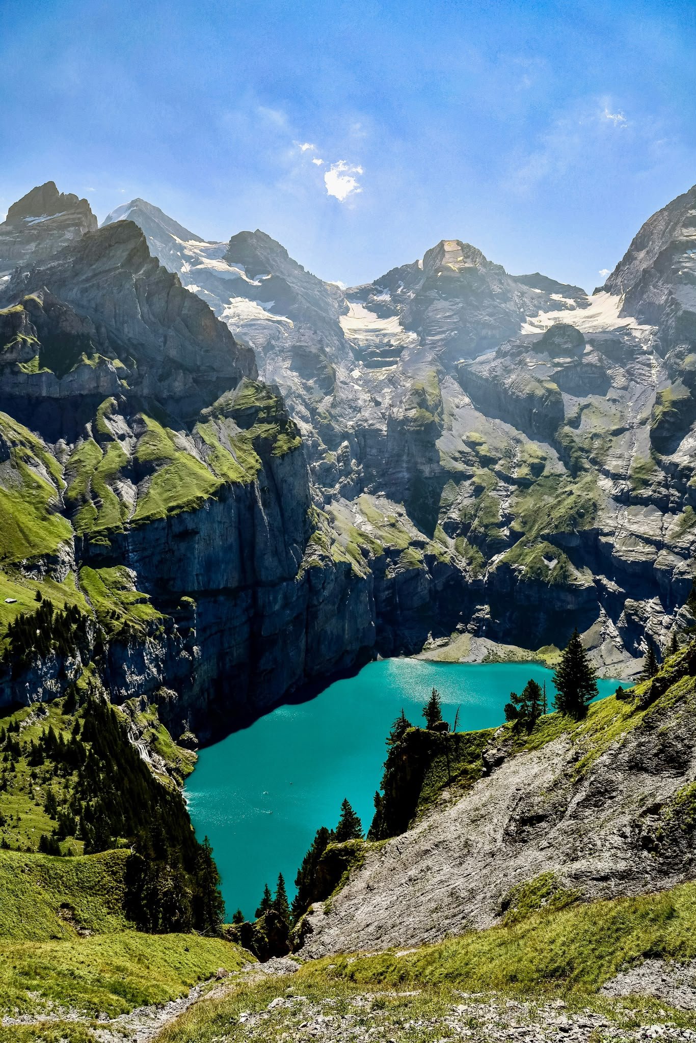 Scenic mountain landscape with snow-capped peaks, a turquoise lake, and green forests under a blue sky.