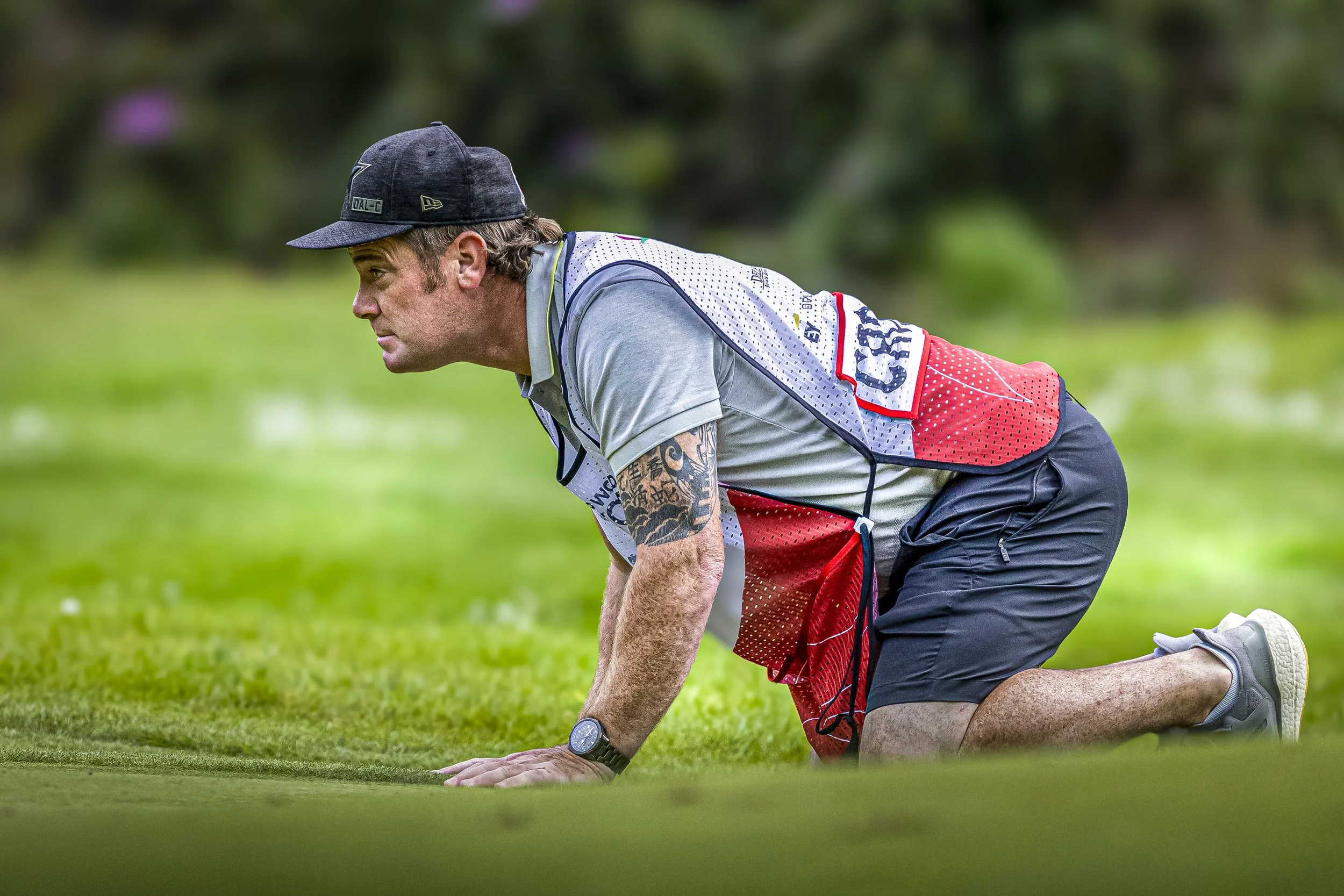 A man in athletic attire on a golf course, positioned on his hands and knees, preparing for a putt.