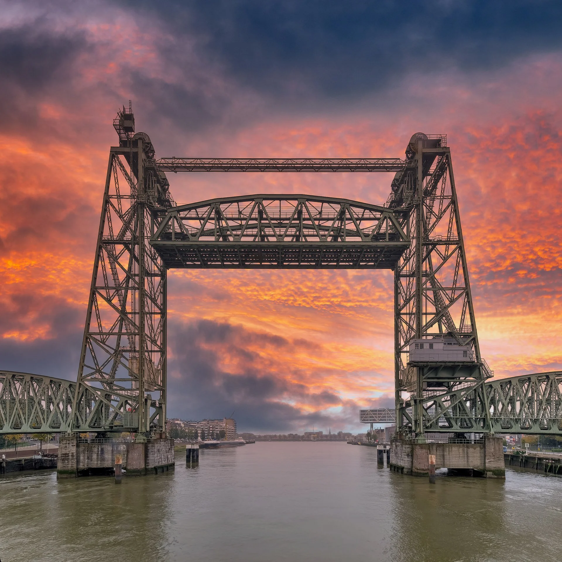 A bridge over a river during sunset with a colorful sky filled with clouds in shades of pink, orange, and purple.