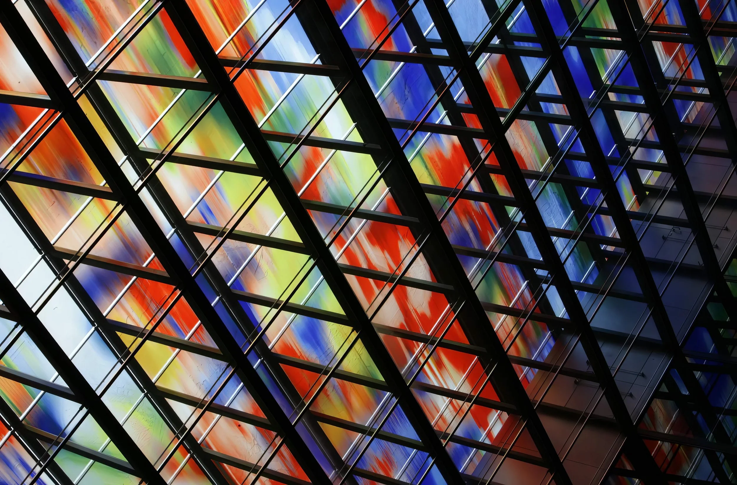 A modern building facade featuring colorful abstract art panels, framed by black metal beams forming a grid pattern.