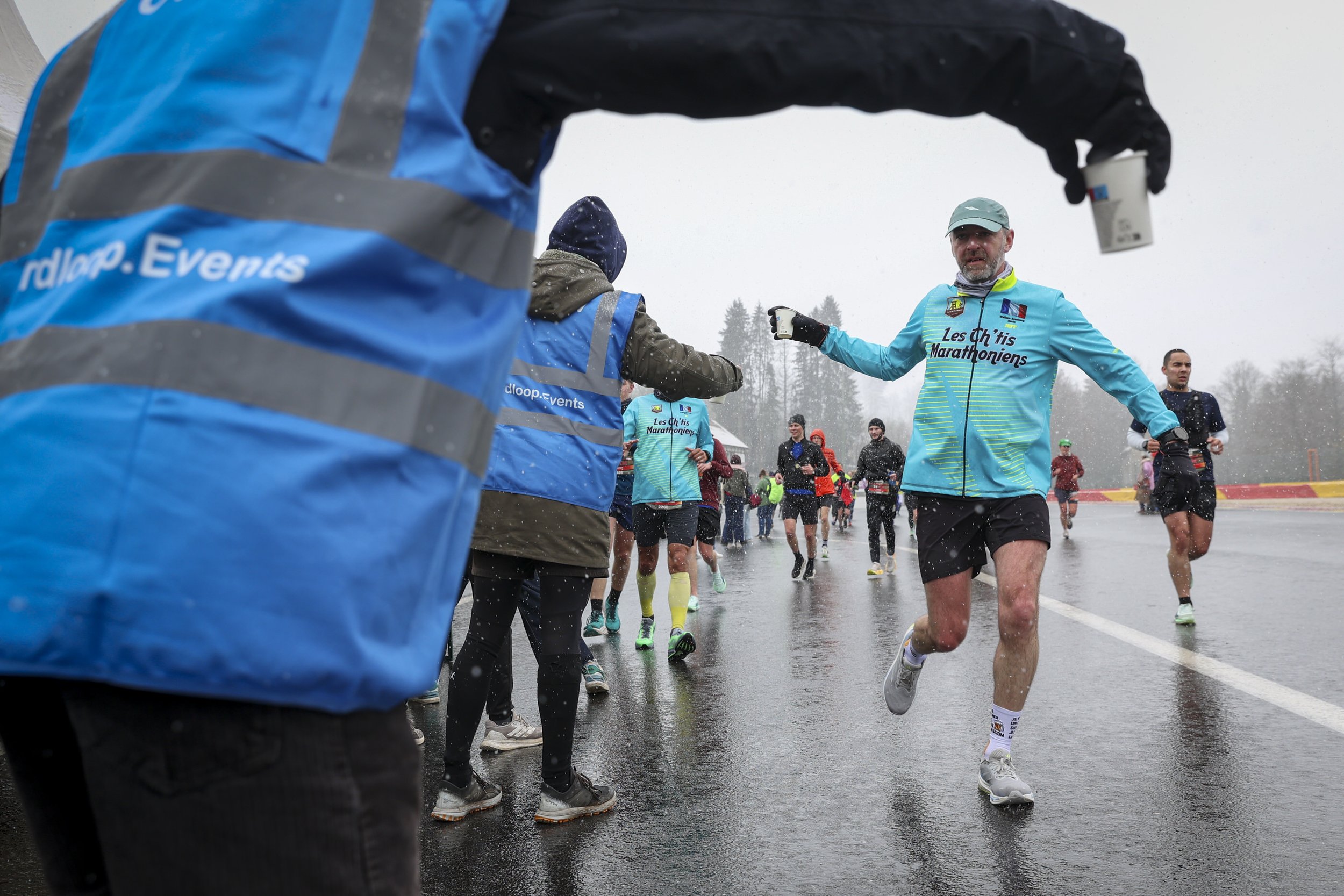 Marathon runners participating in an outdoor race in rainy weather, with spectators and race officials on the side.